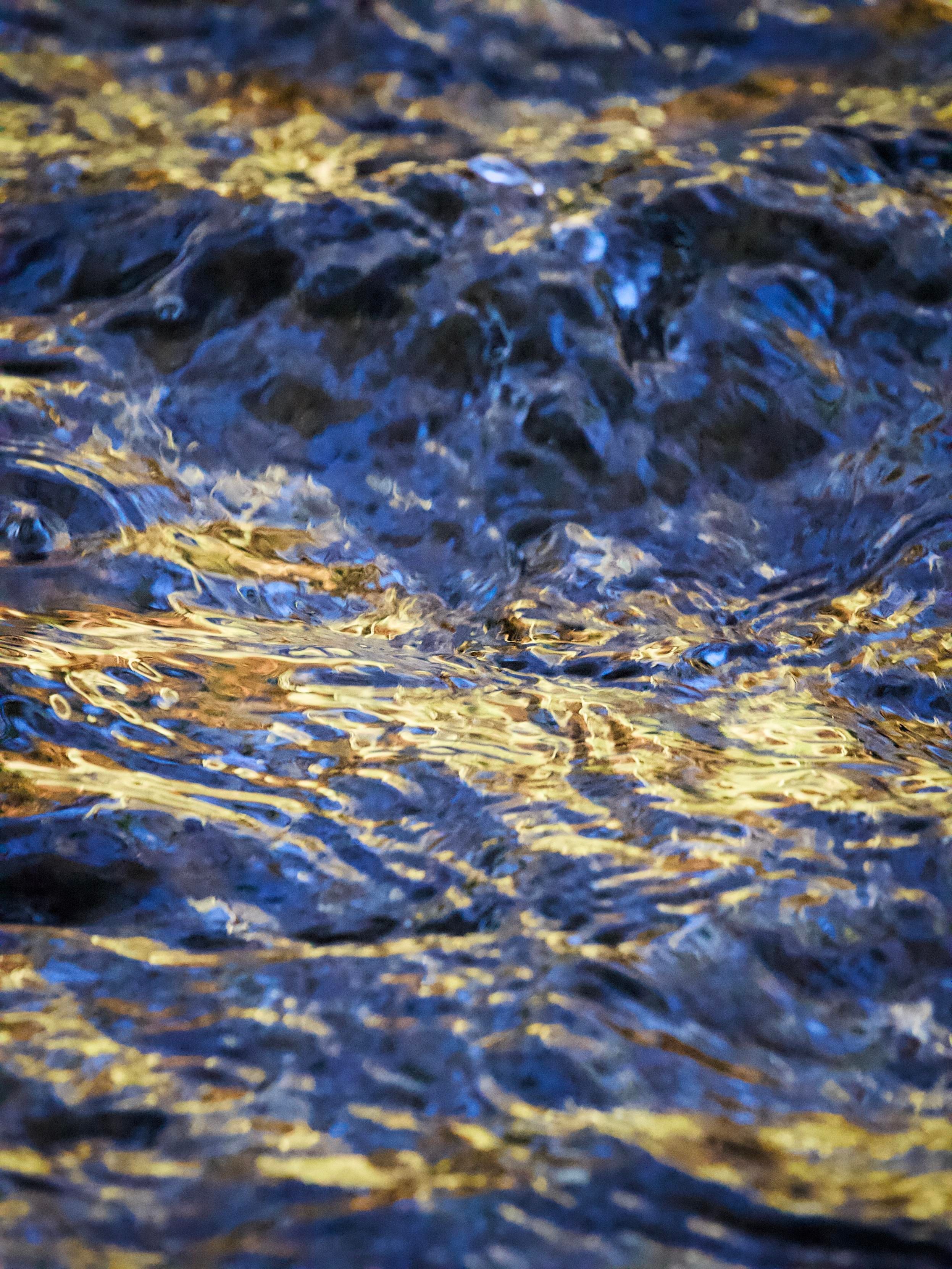 Ripples and reflections in a fast-moving stream create beautiful golden and blue colours and textures when low winter sunlight catches the surface of the water