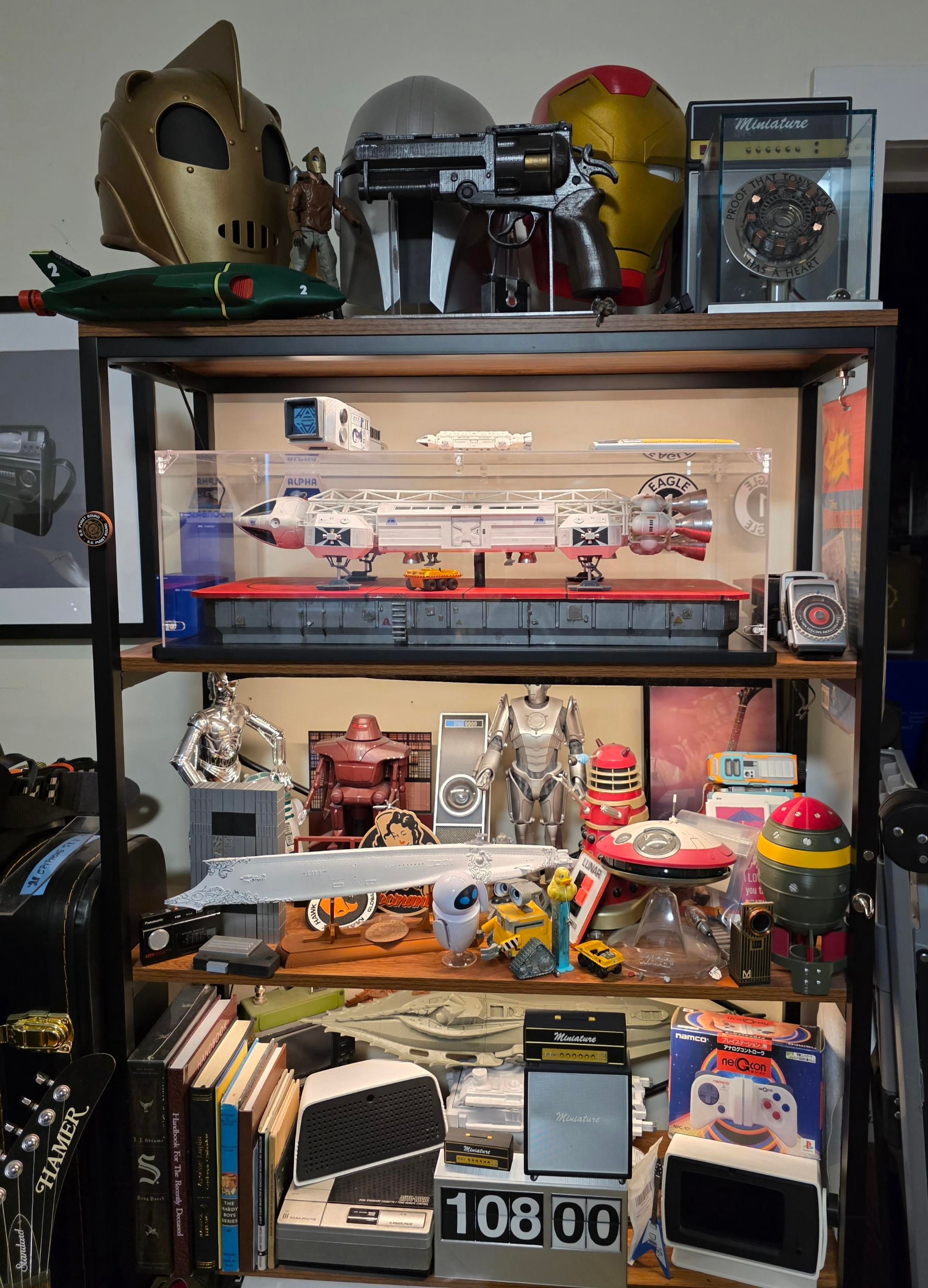 Shelves full of prop replicas, most sci-fi related but not all. This shelf also has helmets from the rocketeer, the mandalorian, and iron Man