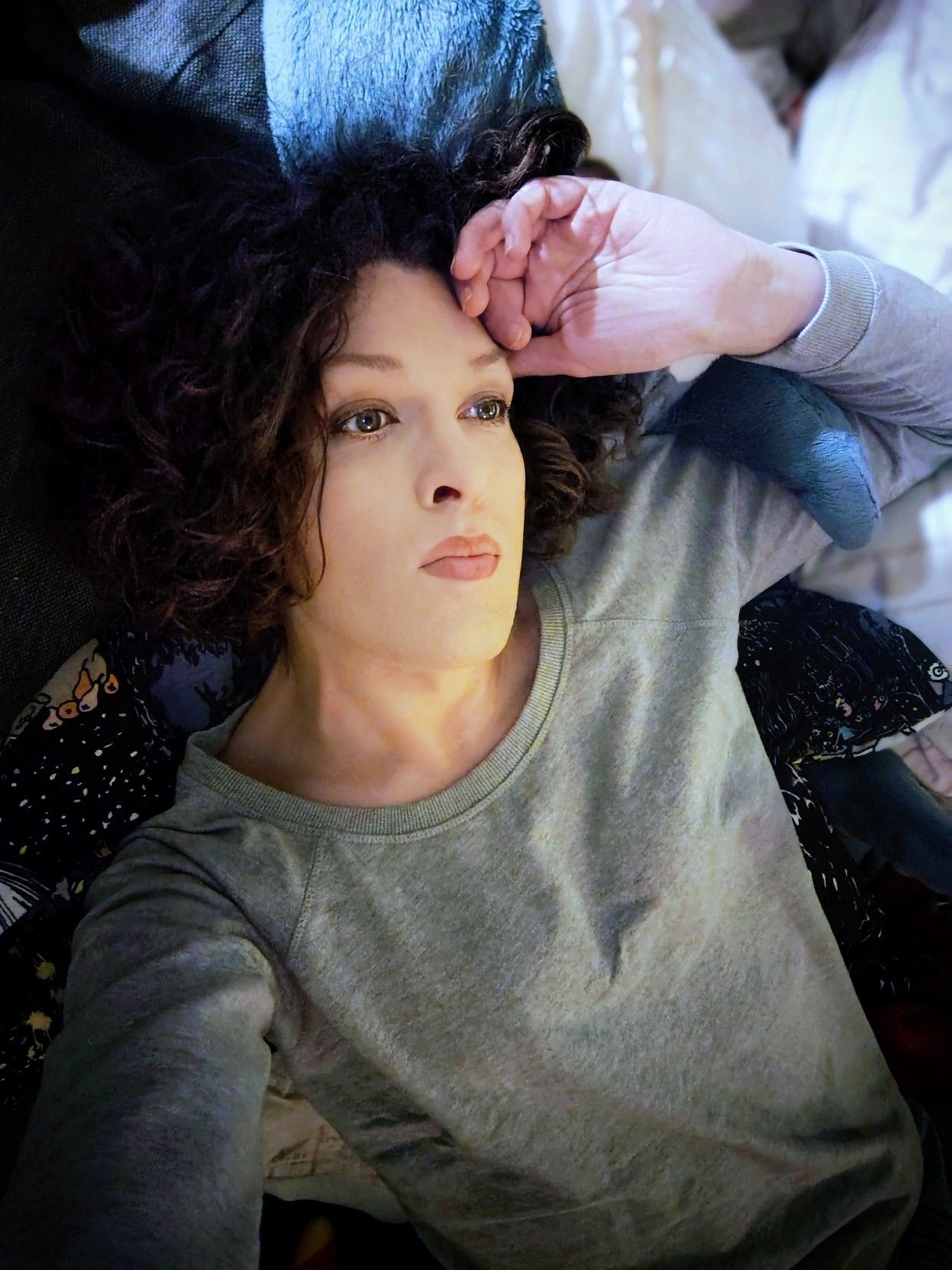 me on my back in bed, a distant stare at the ceiling, wearing grey sweater, with a shark plushie as a headrest, my left hand resting on my forehead