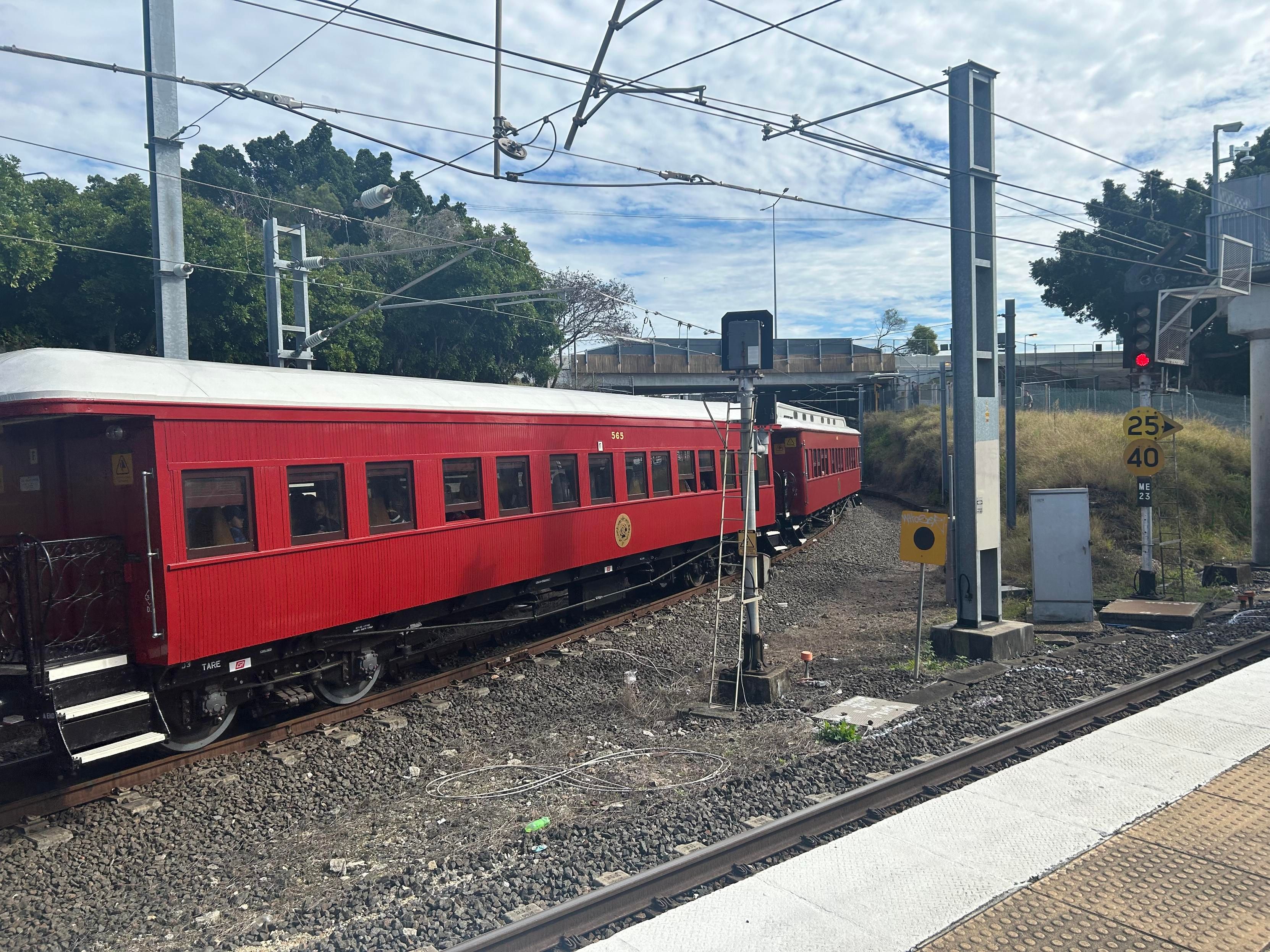A red wooden passenger carriage passes by the camera, the steam loco hauling it has just disappeared around the corner 