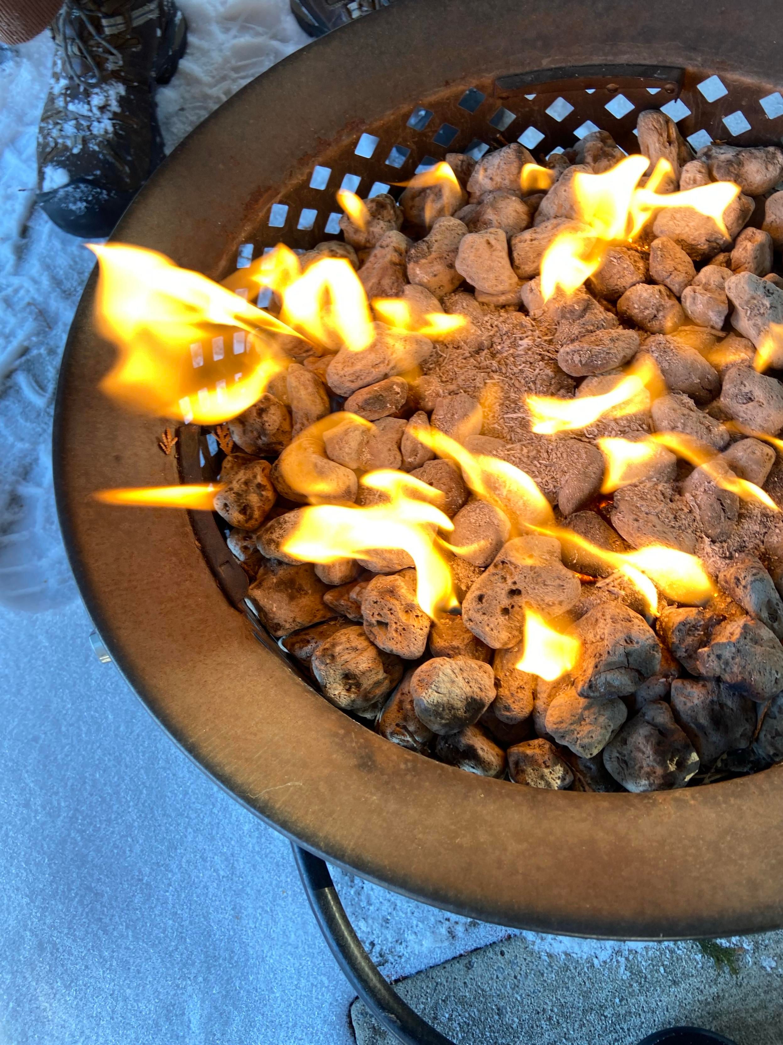 Flames in a small propane fire pit. A person's snowy boot is visible at the upper left. 