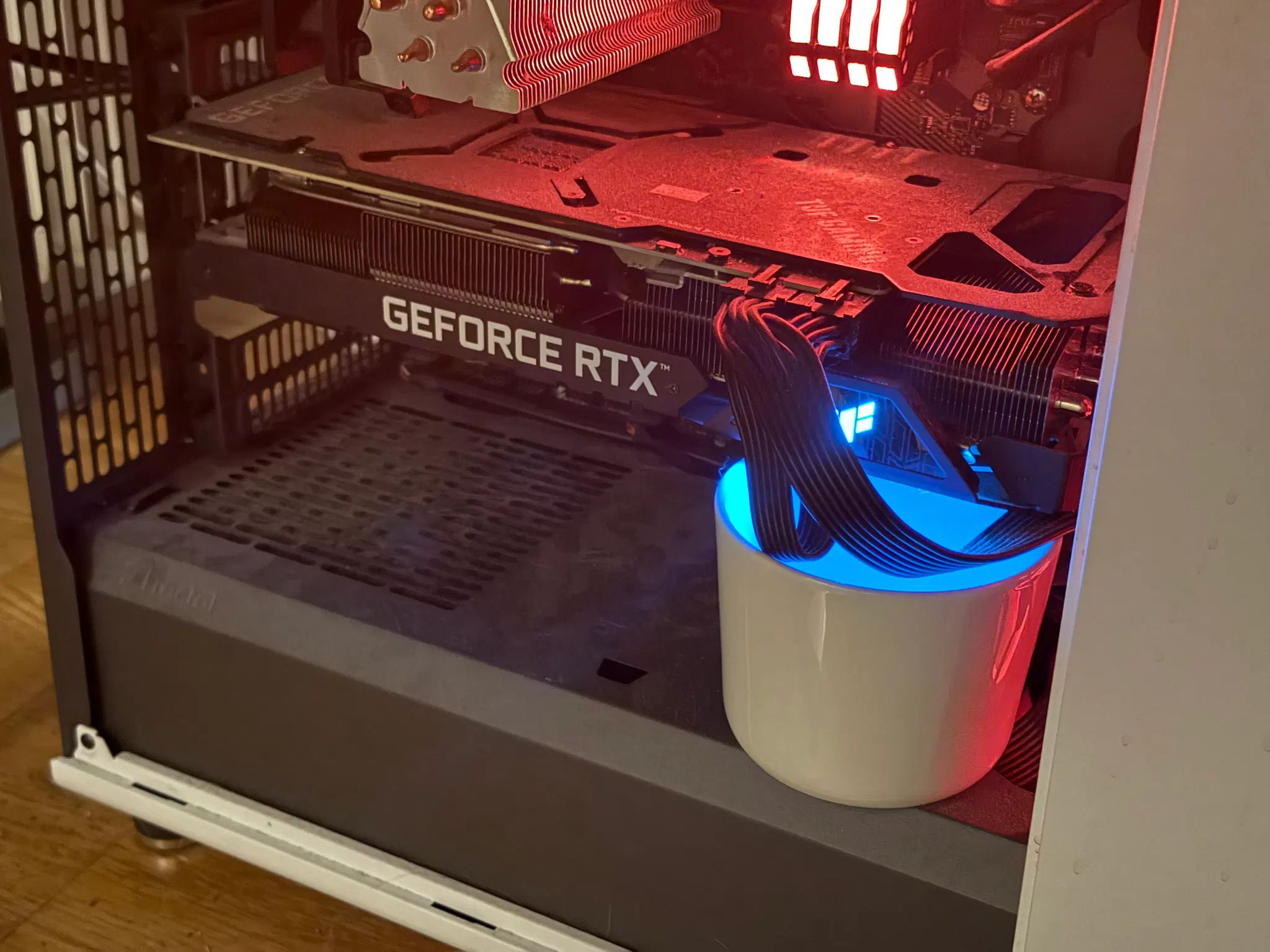 a photo of a computer case with a ceramic mug illuminated by RGB lights sitting snugly under a GPU