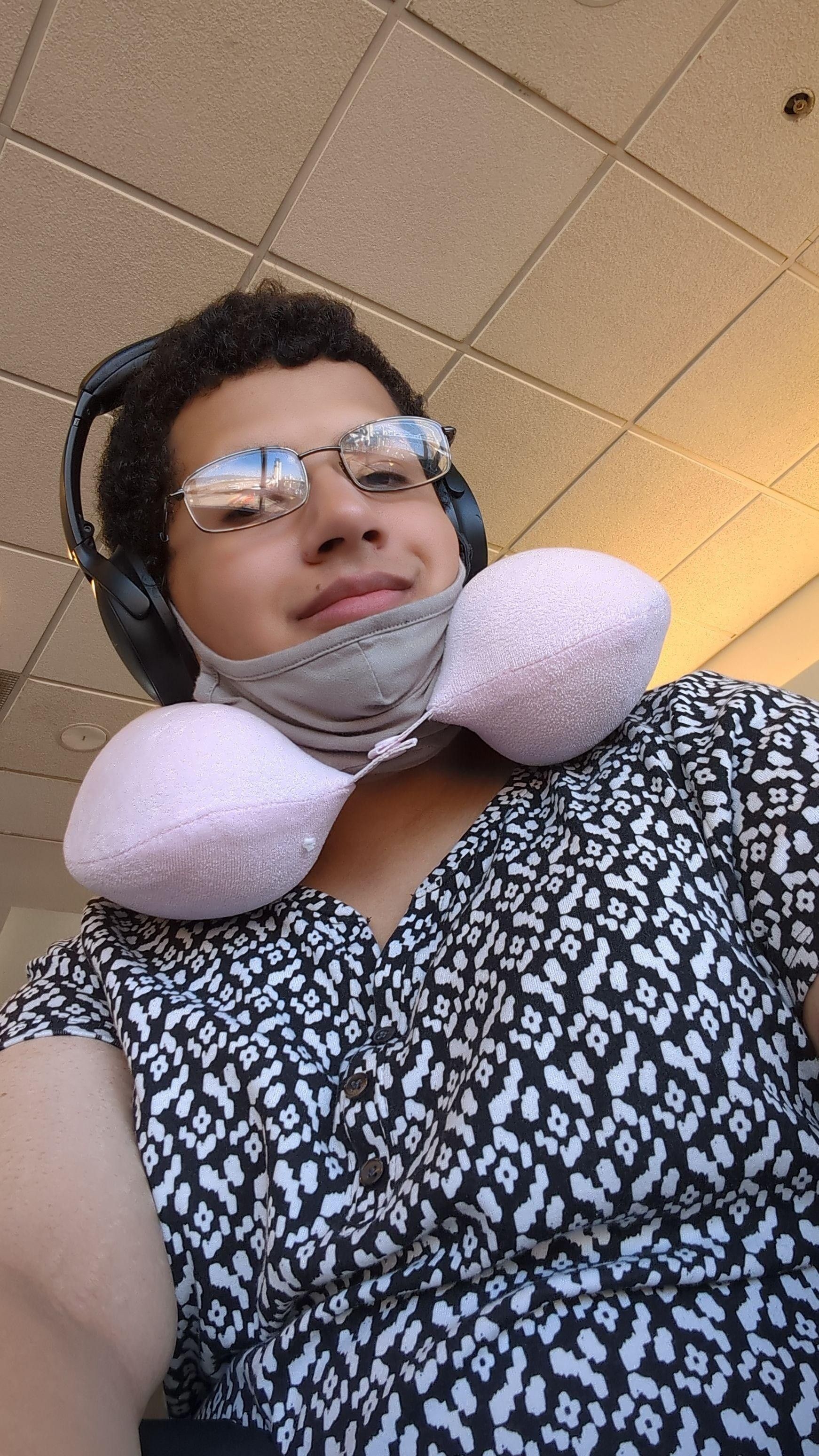 Jo wearing a pink travel pillow around her neck. She's wearing a black and white shirt.