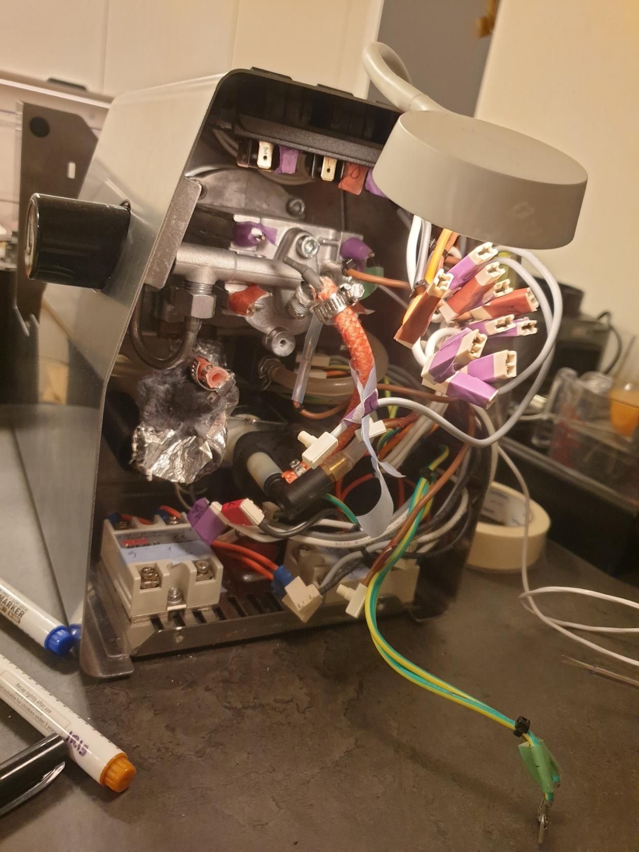 Interior of the espresso machine lying on its side and with a gabillion cables exposed, about half disconnected and labeled with washi tape.