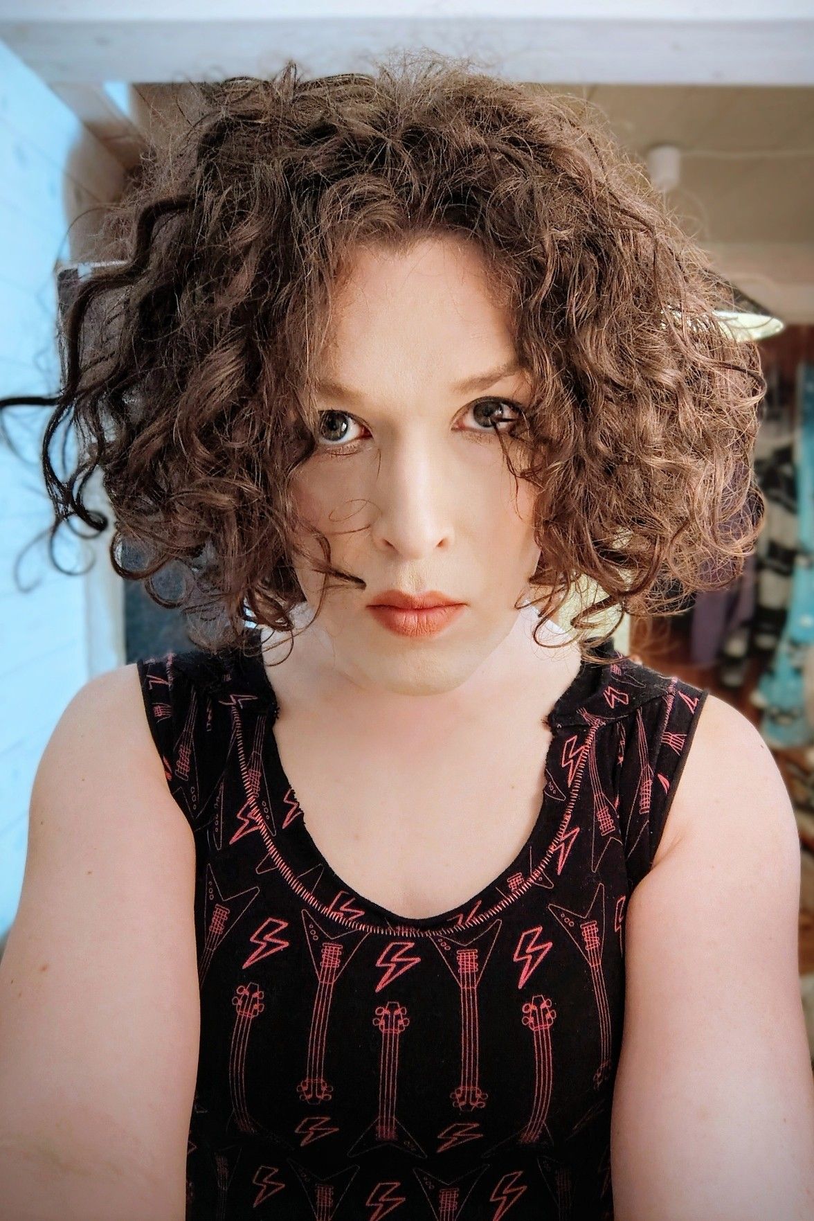 head and shoulders selfie, tight black top with lots of electric bass guitars and flash symbols on it. looking seriously (and cutely) into the camera