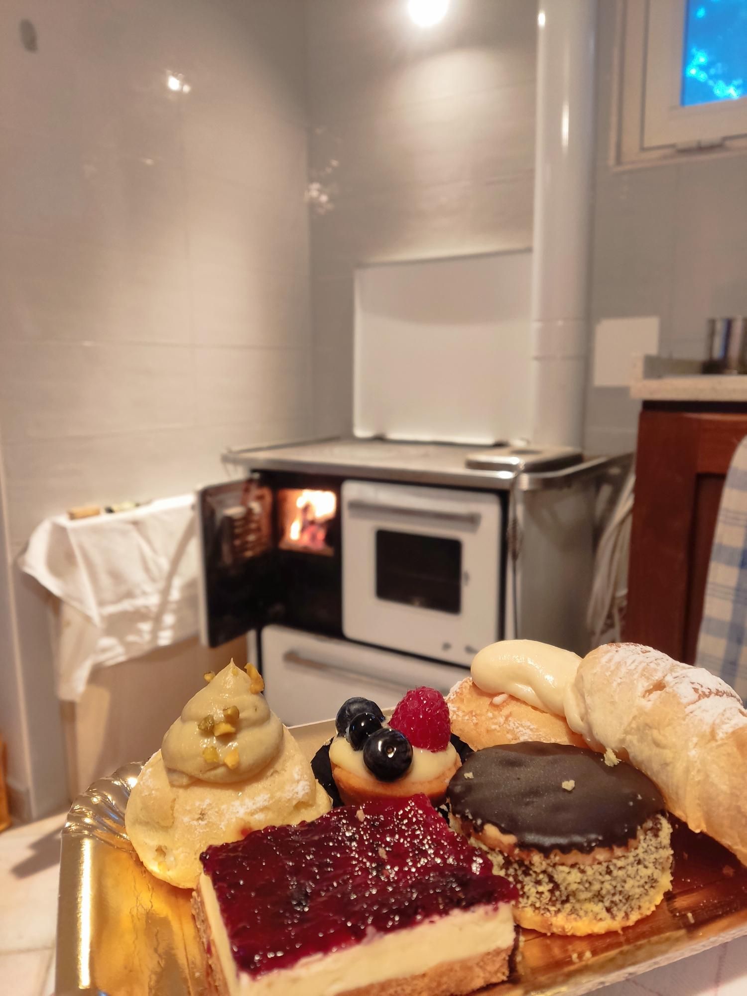 angoluno di una cucina con, sullo sfondo una cucina economica con lo sportellino aperto per mostrare il fuoco acceso e in basso, in primissimo piano, un vassoio con 6 mignon diversi