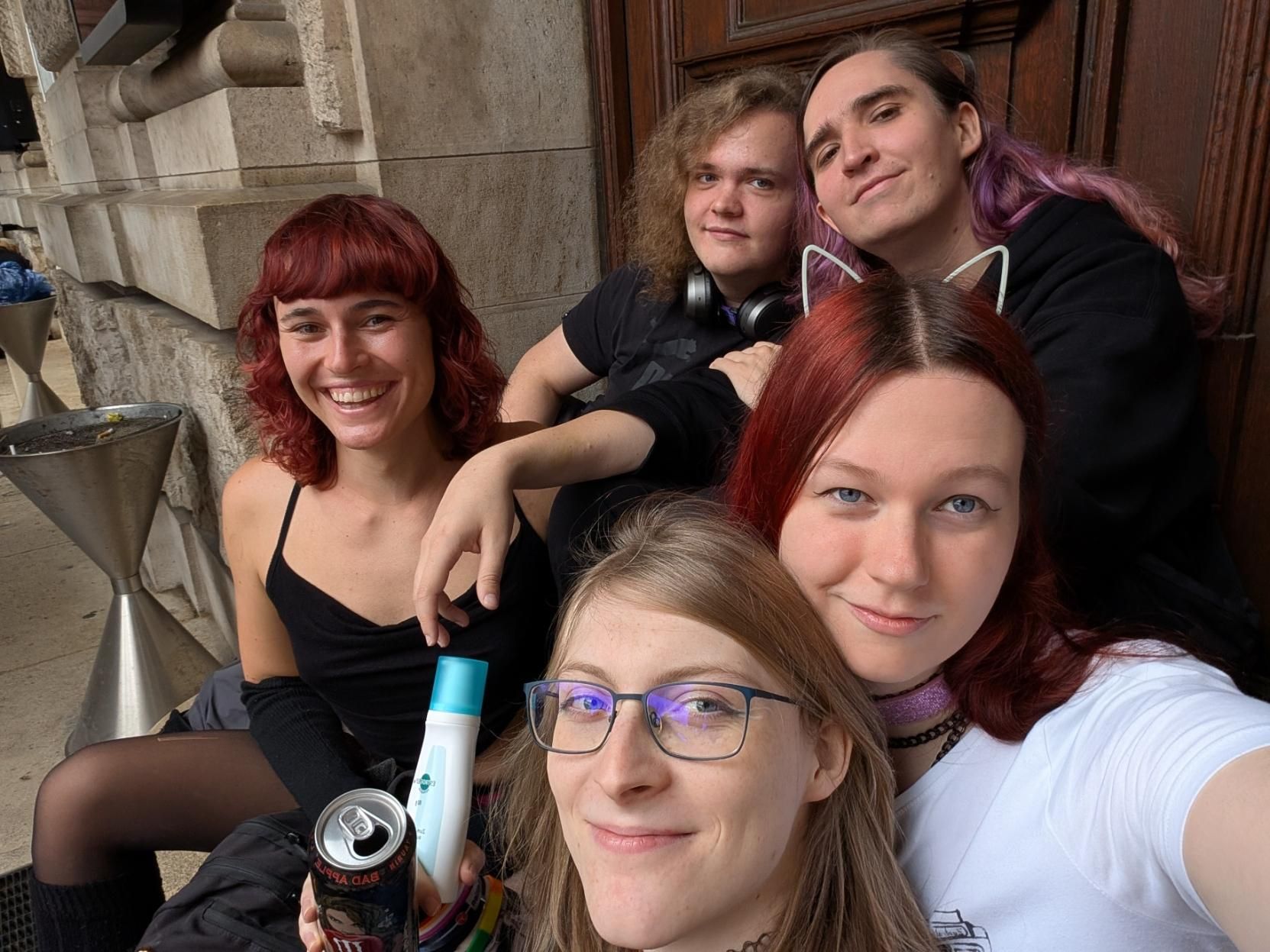 A bunch of people sitting on stairs, some wearing cat ears, also depicted: estradiol cream & energy drink