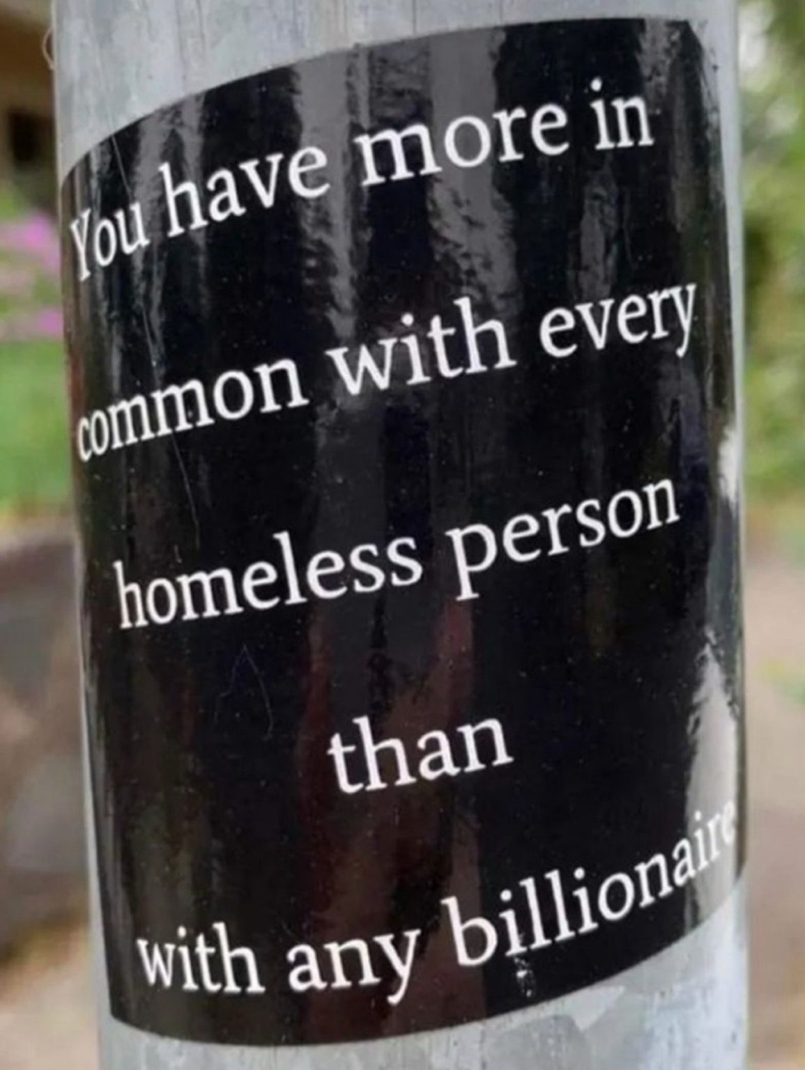 Schwarzer Sticker auf einer Laterne (Nahaufnahme) auf dem Sticker steht in weiß „you have more in common with every homeless Person than with Any billionare“