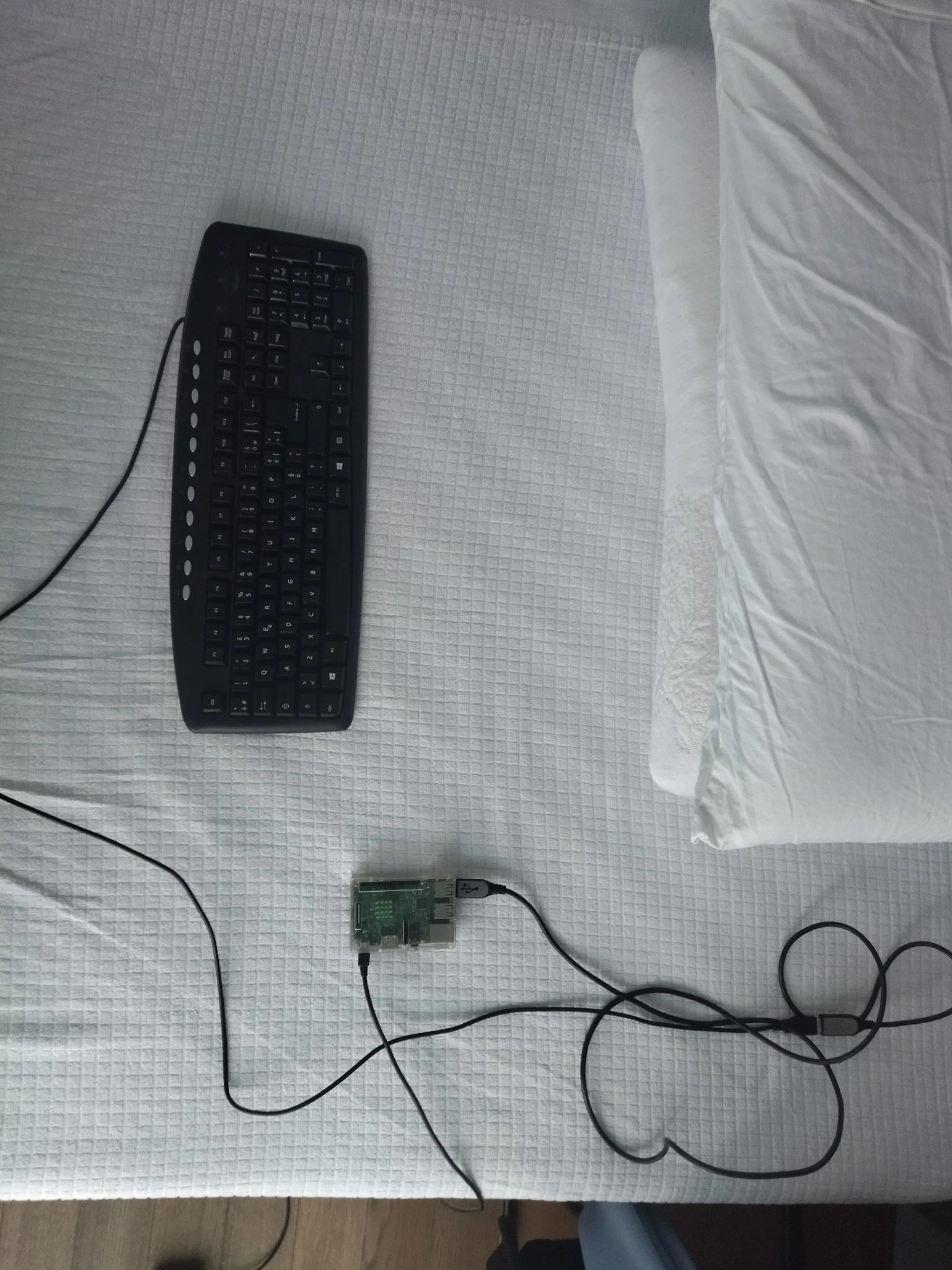 Foto della tastiera appoggiata sul mio letto da rifare, collegata al Raspberry Pi 3 appoggiato ugualmente sul letto