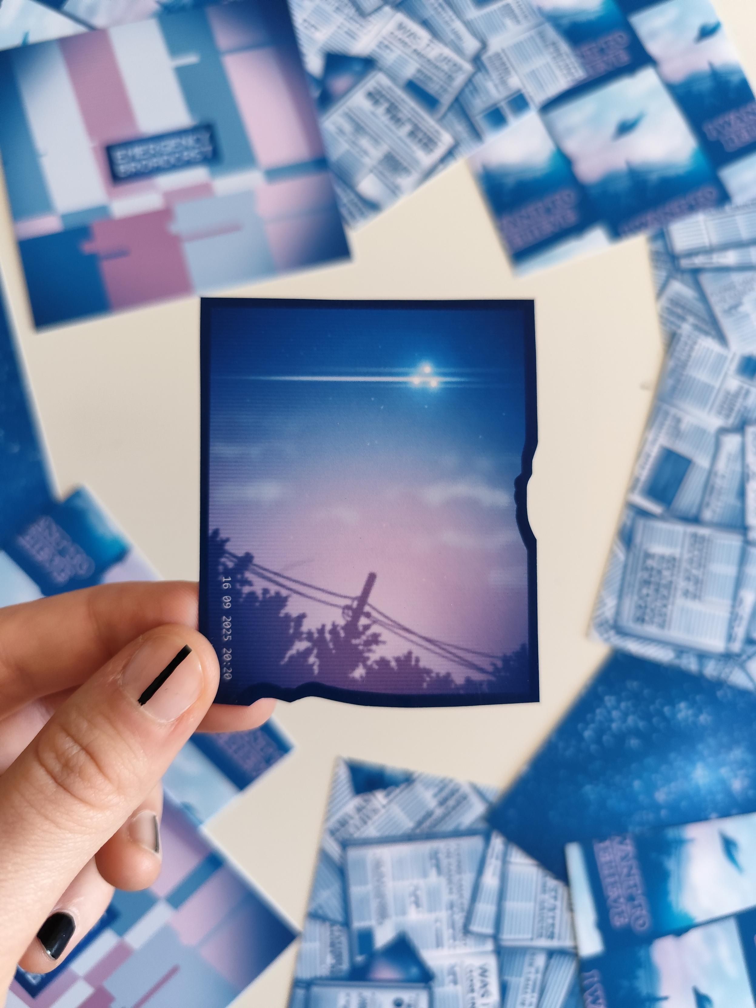 hand holding up a sticker of a made-up drawn UFO sighting showing a craft with 3 bright lights in the sky
