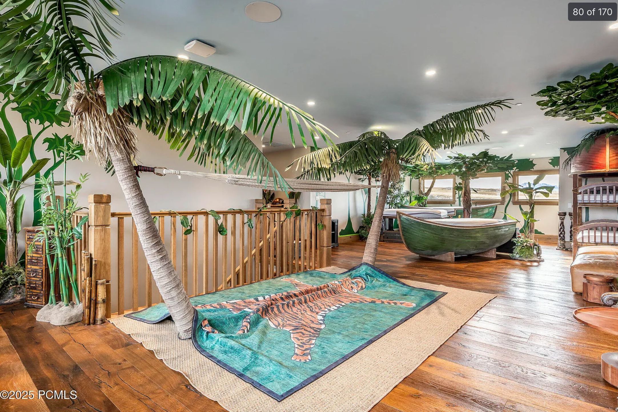 An indoor area at the top of some stairs with timber flooring, fake palm trees, a row boat, and a carpet with a fake tiger pelt
