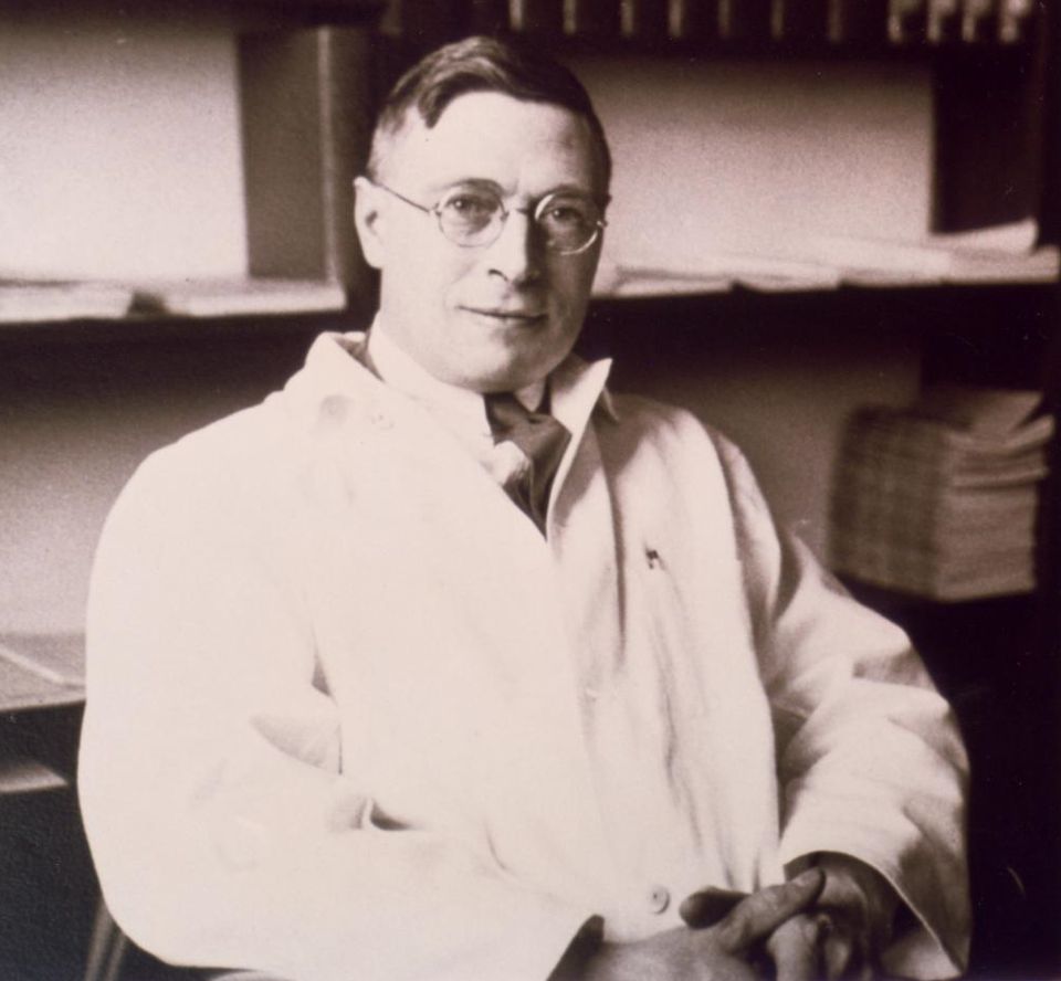 J. B. Collip in his office at McGill University.

Collip is seated and photographed from approximately chest level up. He wears round wire-rimmed glasses and has neatly combed dark hair parted to the side, styled in the fashion typical of the era. He is dressed formally in a white laboratory coat over a shirt and tie.

https://en.wikipedia.org/wiki/January_1922#/media/File:J._B._Collip_in_his_office_at_McGill_University_ca._1930.png