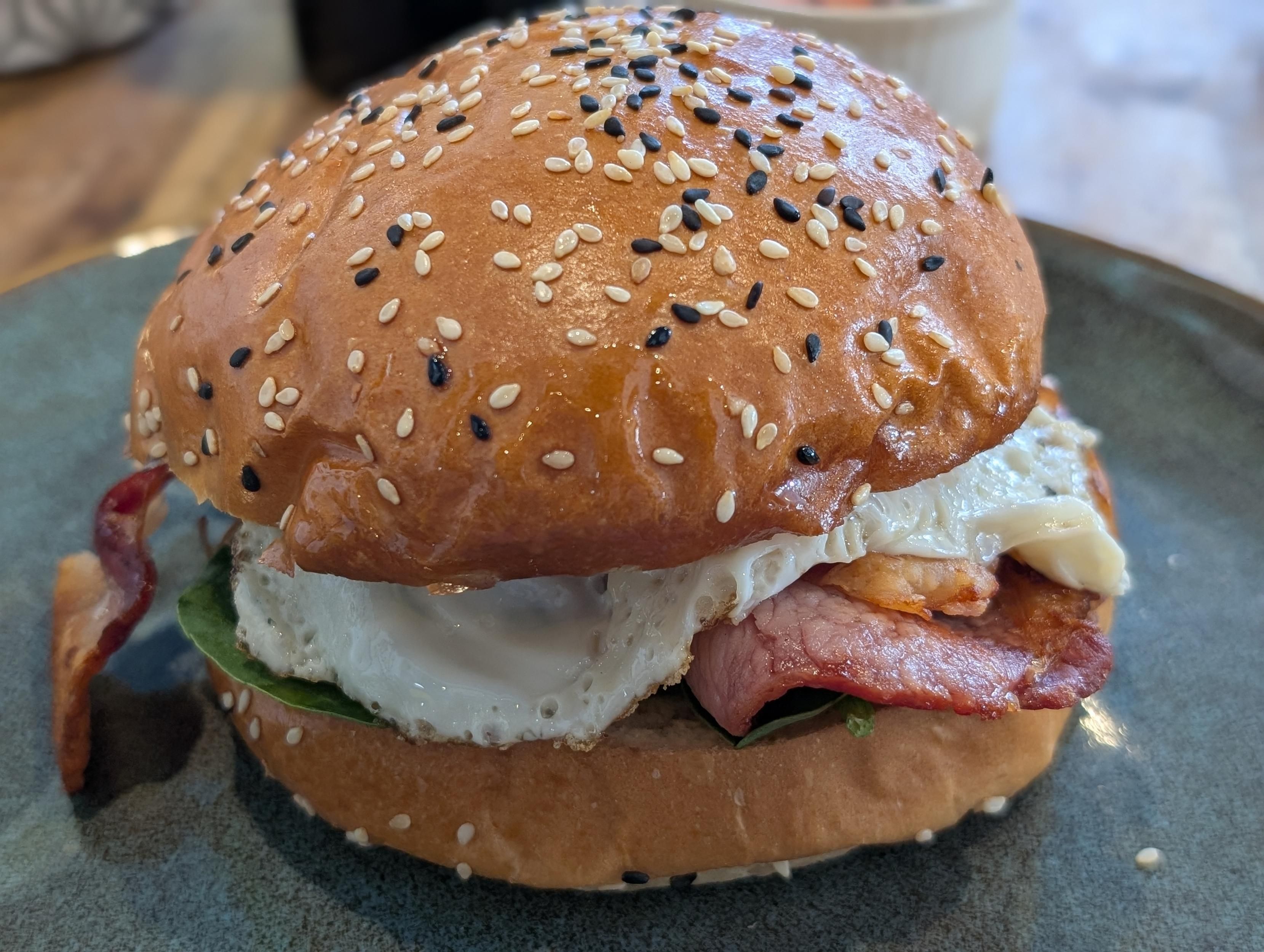 Bacon and egg roll with spinach, all between a bun with black and white sesame seeds