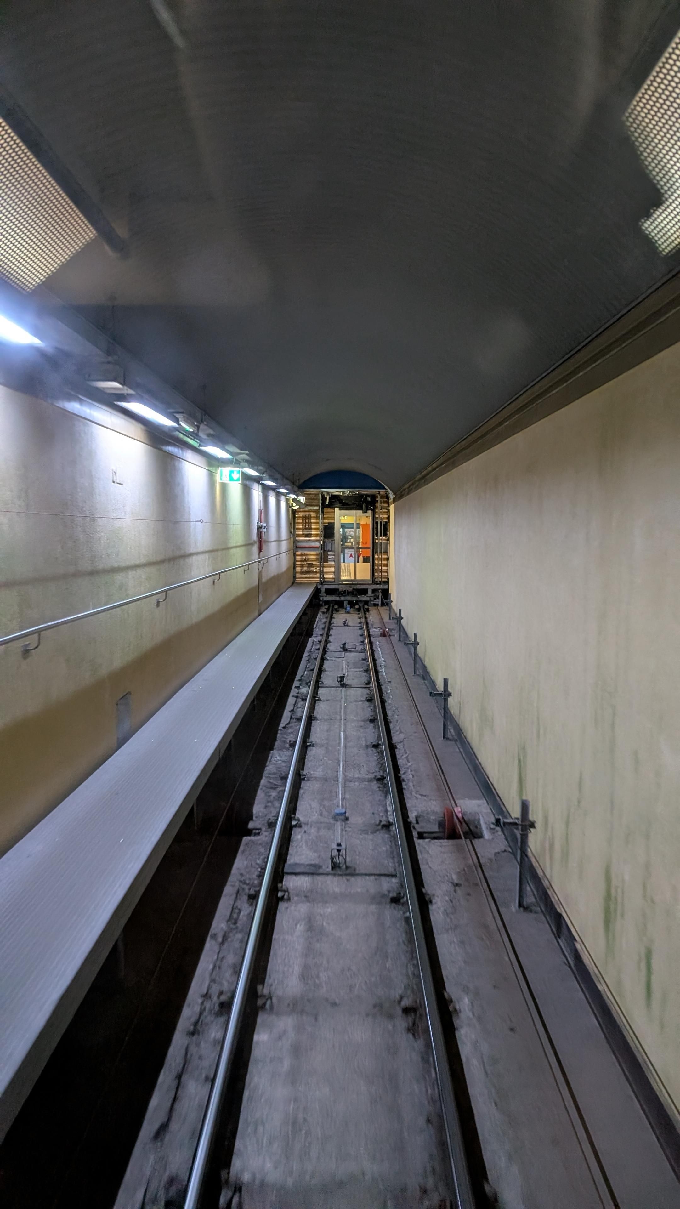 Straight underground tracks leading to a glass door at the end of the tracks, a waiting room for passengers behind it