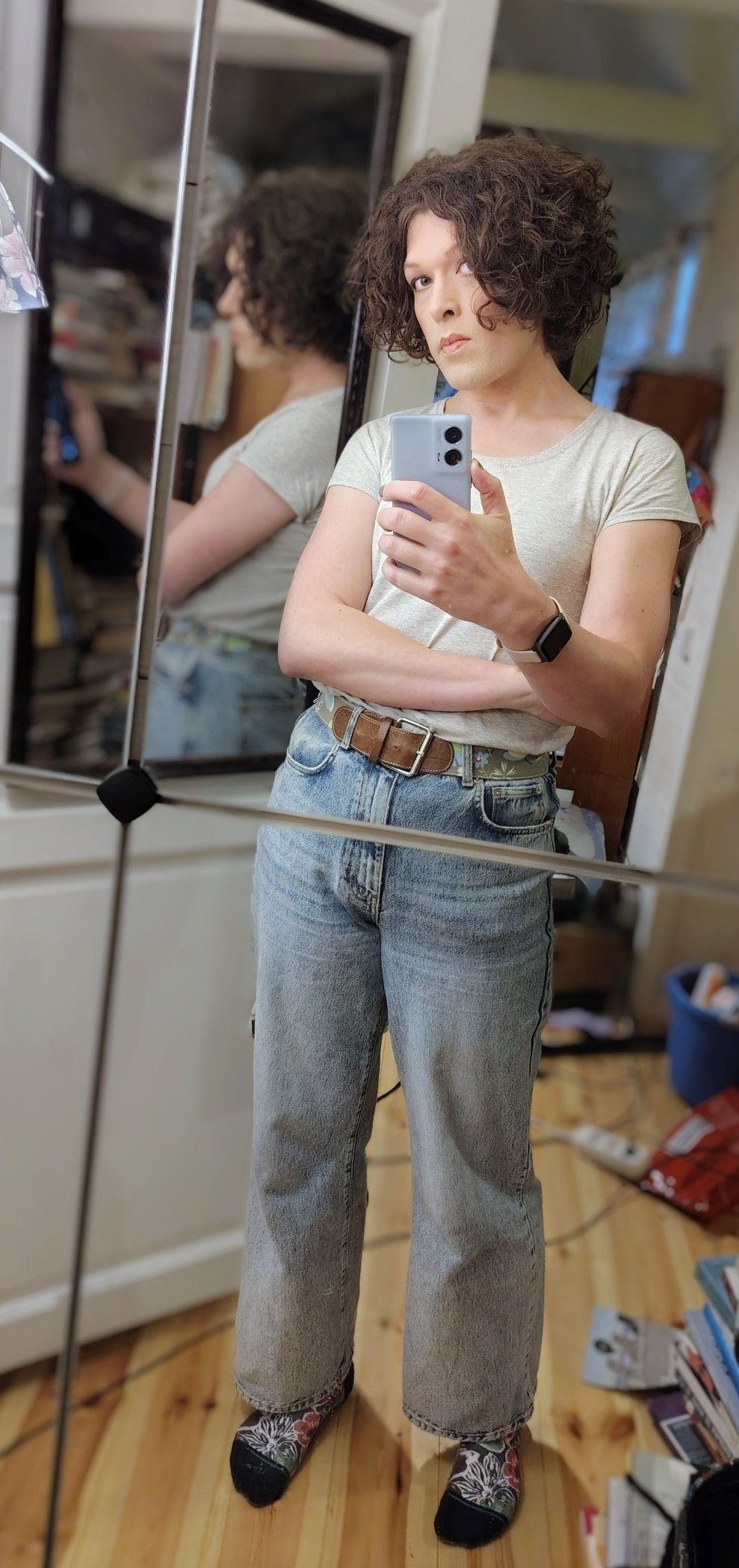 mirror selfie, light grey t-shirt tucked into light blue boot cut jeans, right arm held in front of my tummy, leaning back a bit and putting more weight on my left hip, head tilted to the right with a serious expression