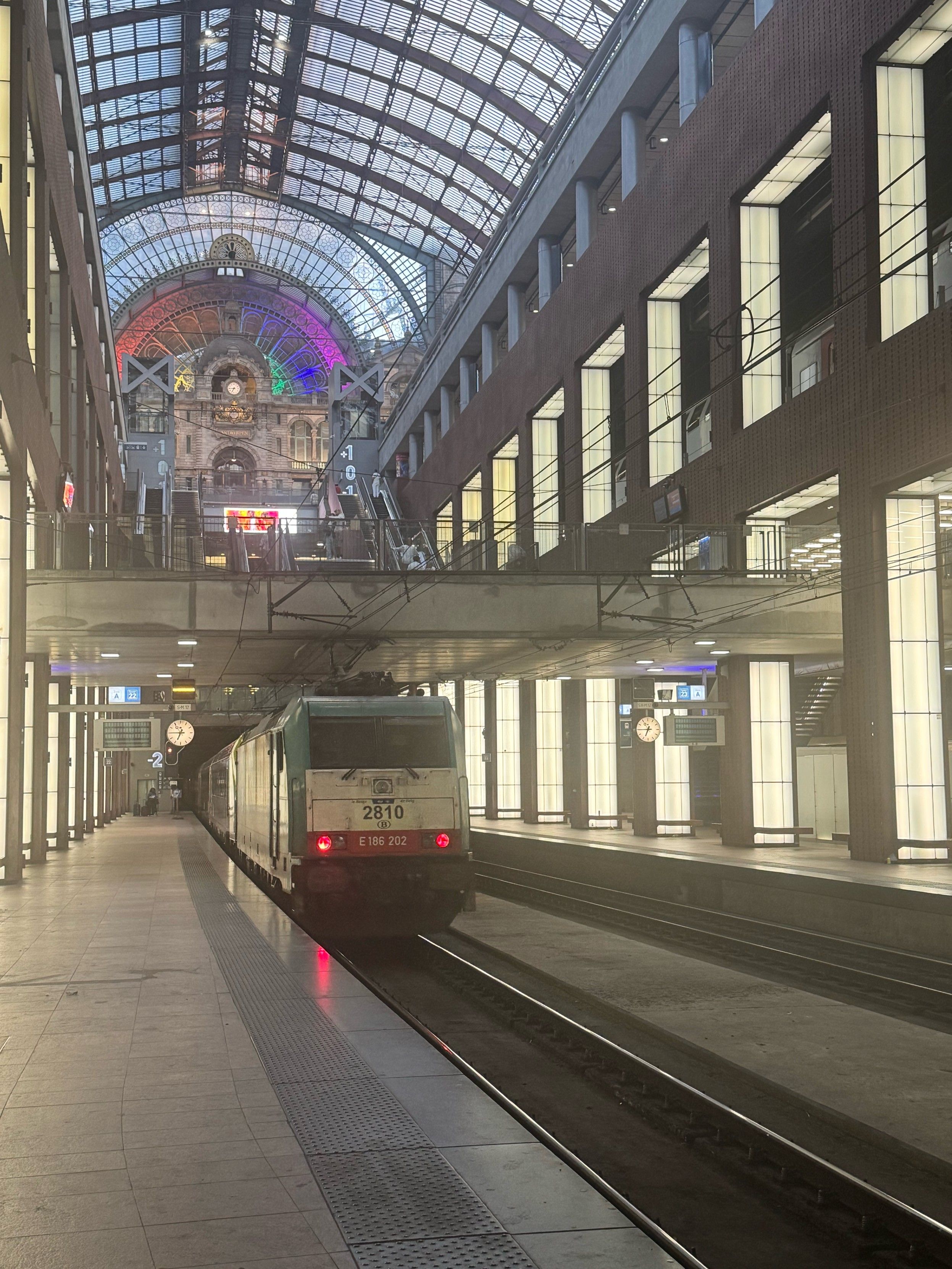 Antwerpen Central Station, a train is departing. On the top there are some headlights showing the pride colors