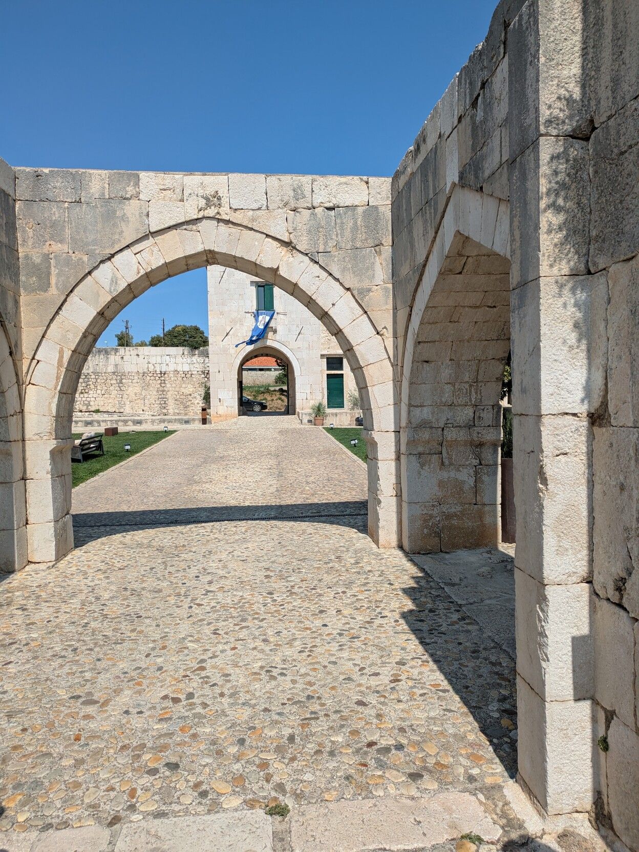 A white courtyard with several pointed archways to the front and to the right. 

Through the front archway, a small square tower can be seen with another pointed archway in the middle. A small blue flag can be seen, hanging from a window on the tower.