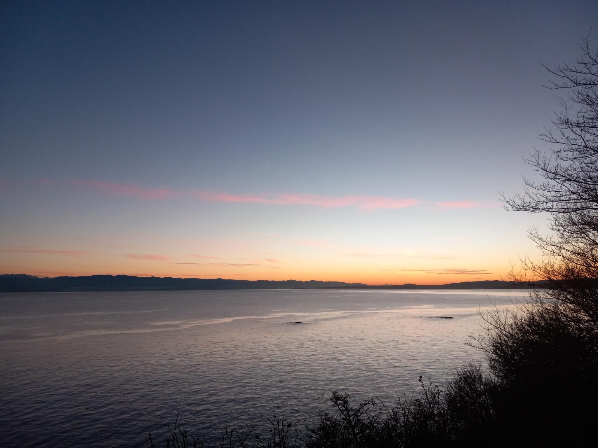 A ridiculously gorgeous view looking across the ocean toward the Olympic Mountains in the US, with the sky dark blue above and orange right above the mountains, with a few pink clouds thrown in for good measure.  If you look very carefully, you can see the teeny tiny crescent moon.