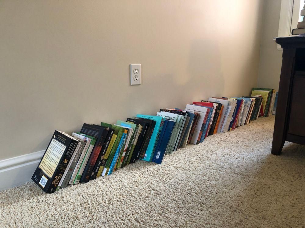 Books lining the floor along the wall 
TBR “pile”
