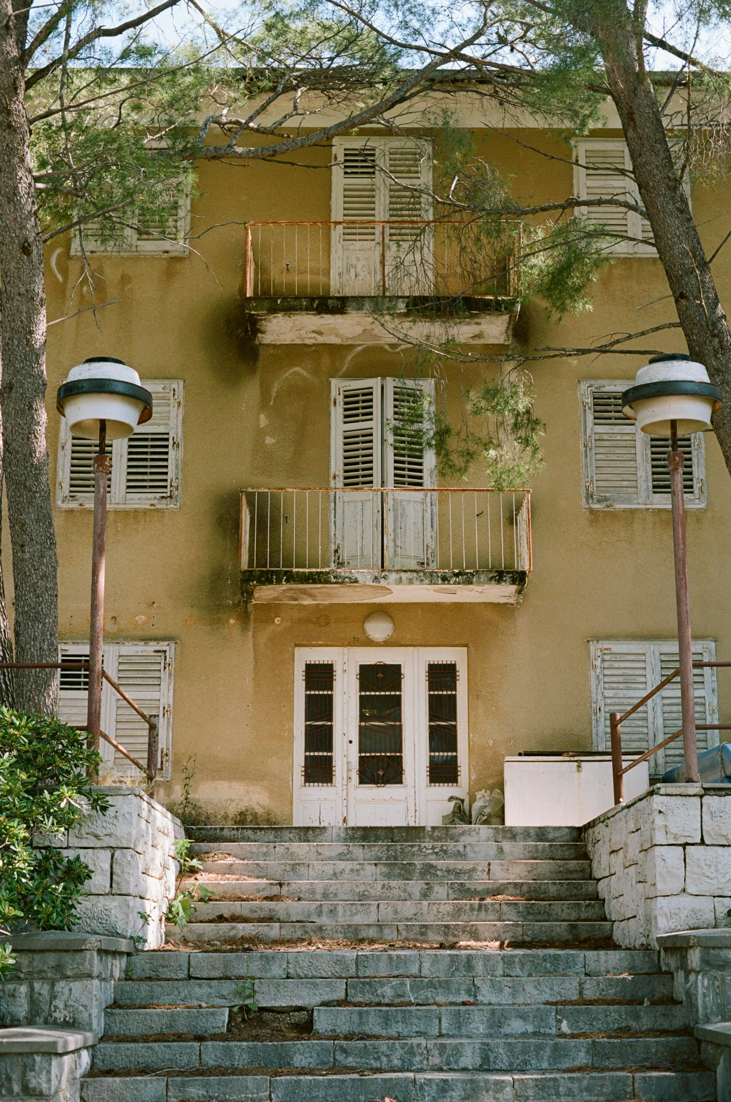 A weathered beige building with closed shutters and a big staircase leading up to it.