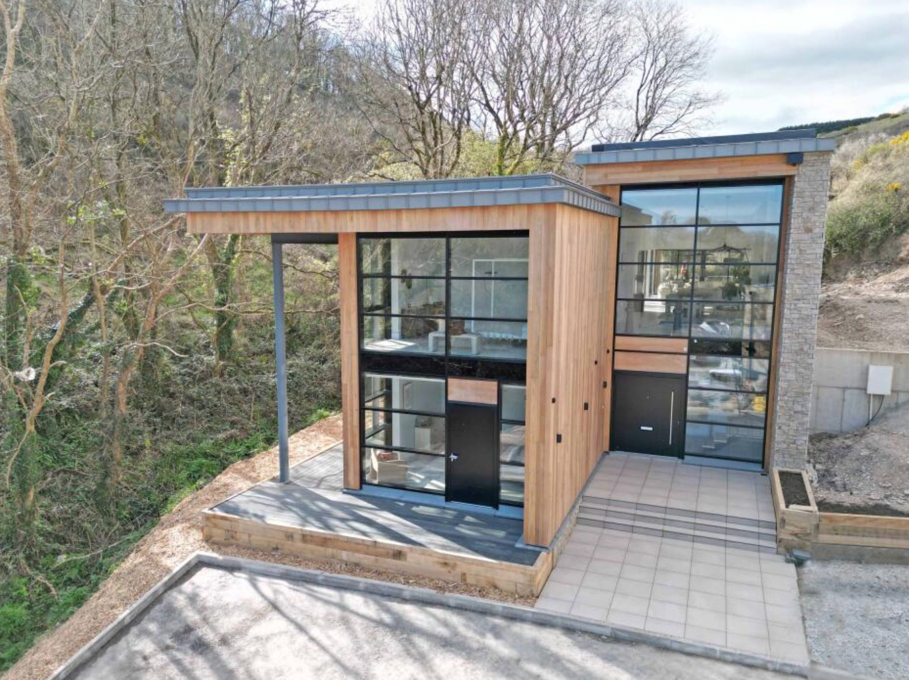 A very modern house made of a lot of glass and timber, but it's right near the edge of a steep drop off. It's not very high up, but still high enough to cause some damage if there were any erosion. 