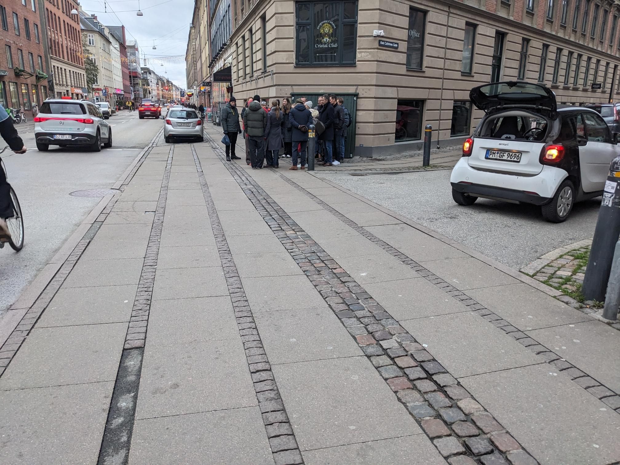 A sidewalk stretches over a street coming in from the side, keeping it's paving and its look over a long distance.