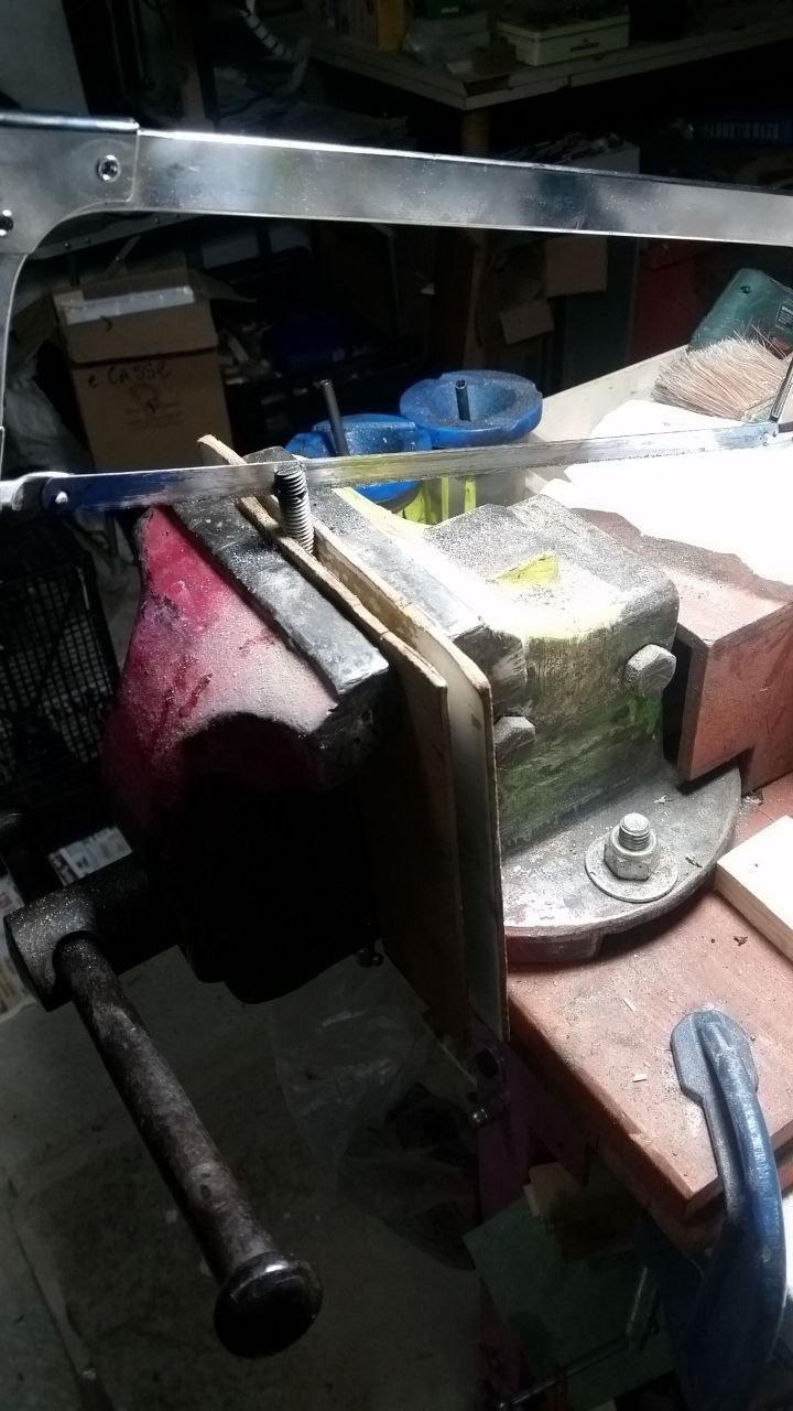 Barra filettata stretta nella morsa grande, con seghetto da ferro in corso di taglio.