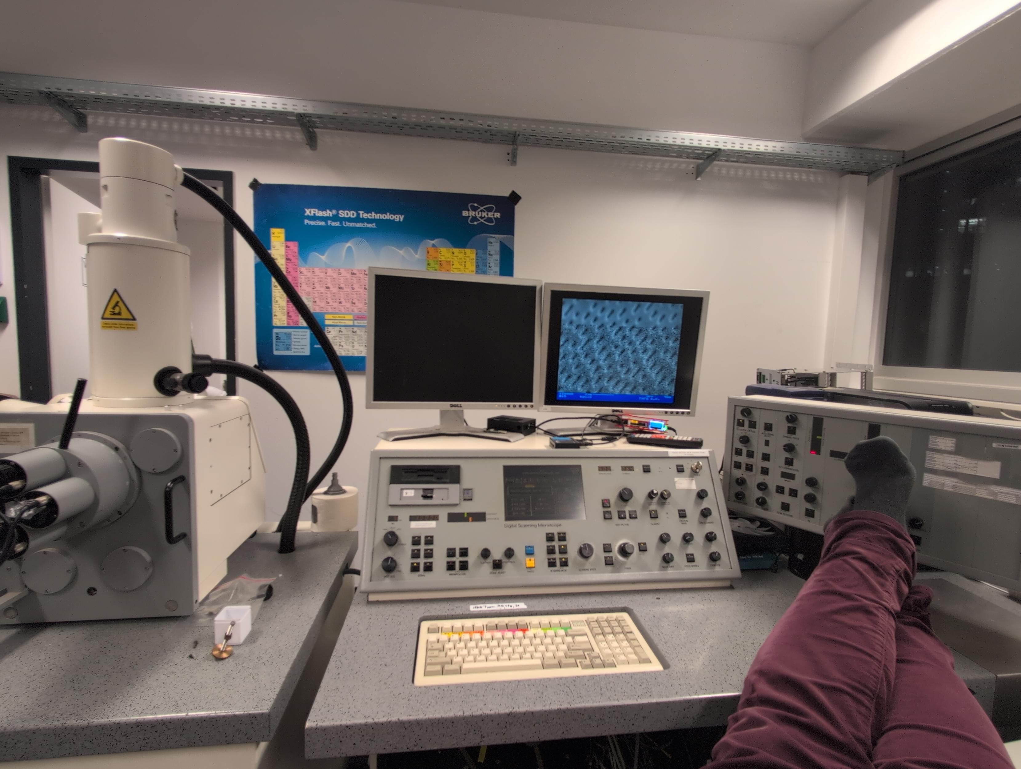 Feet up on electron microscope console. Screens shows DVD pits being imaged.