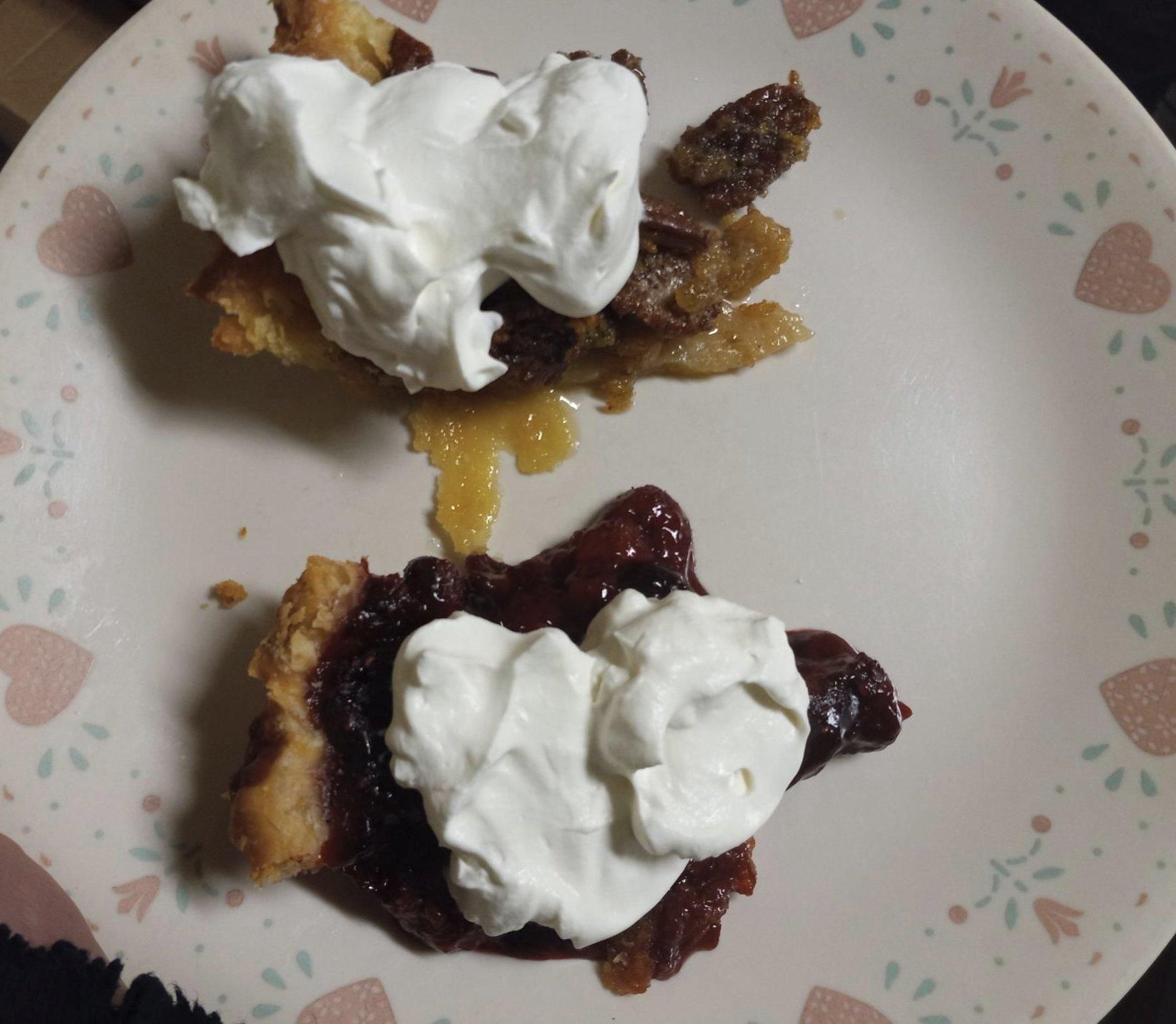 A slice of purplish berry pie and a slide of pecan pie, on a plate, each with a glob of whipped cream on top