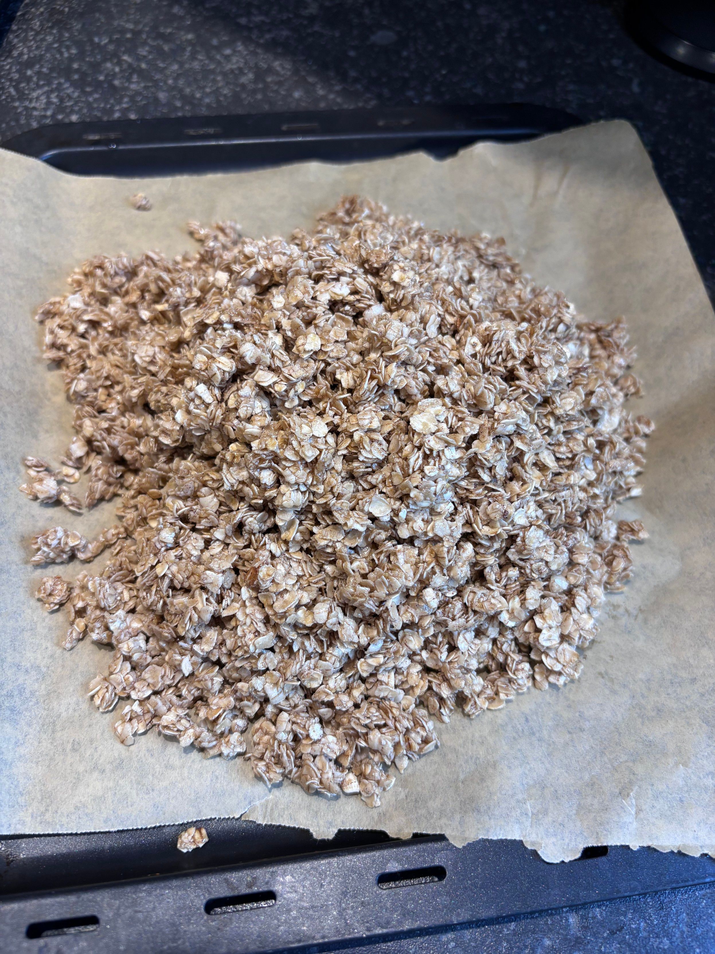 A baking tray lined with parchment paper holding a pile of granola oats.