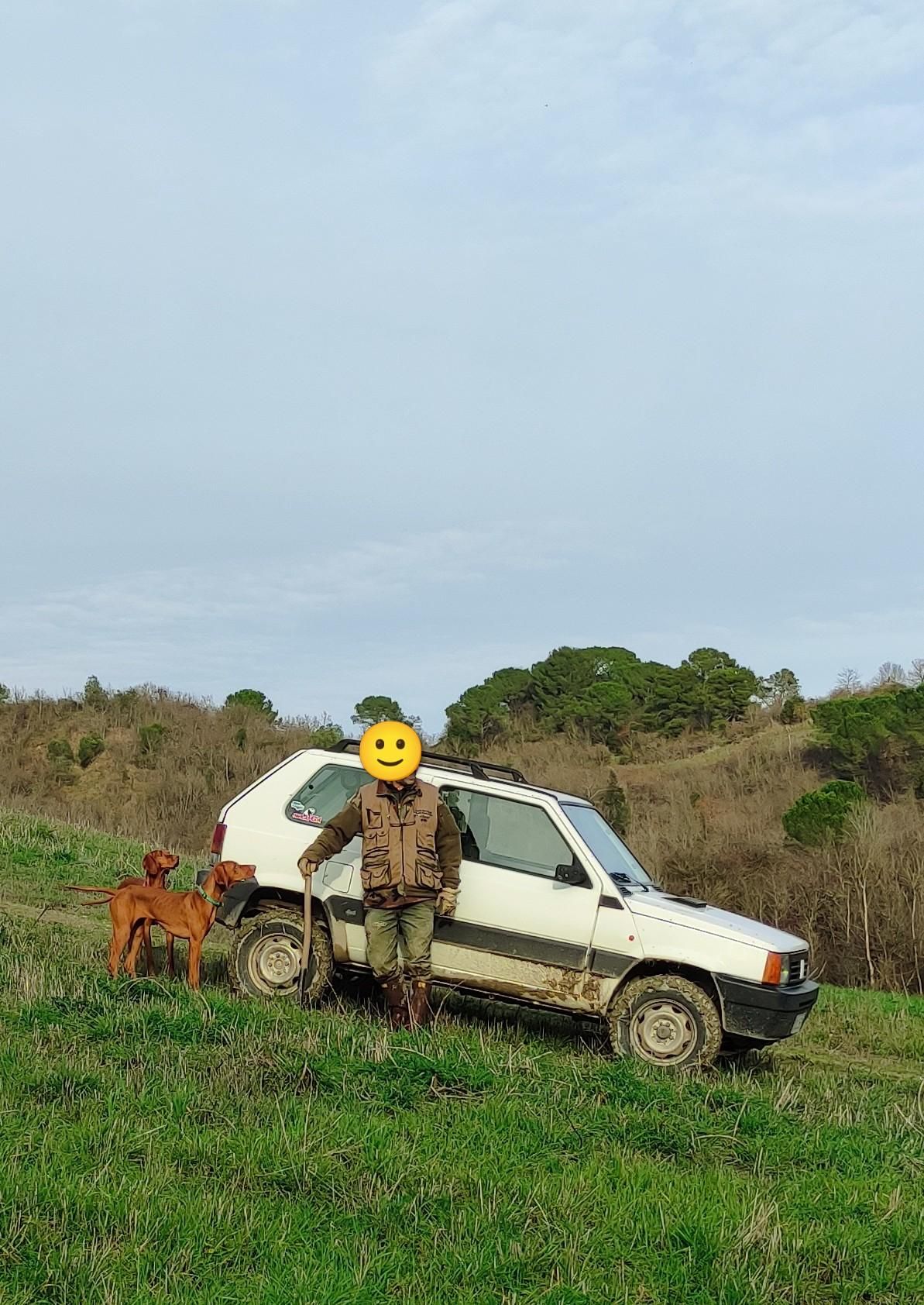 una panda bianca 4x4 su un prato, davanti marito in tenuta da tartufi e le due bionde che lo guardano
