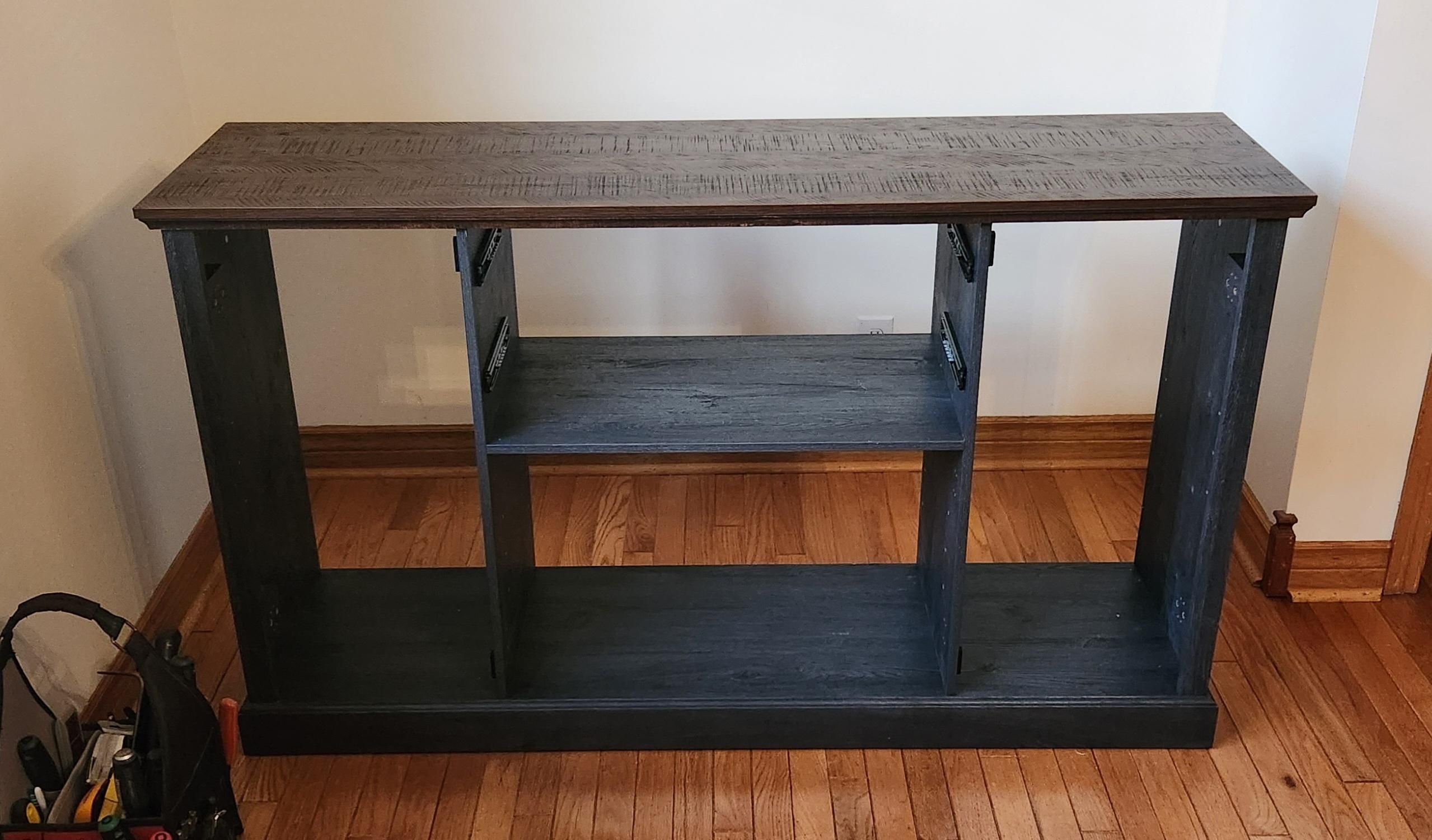 A partially built sideboard.  The bottom, 2 side panels, two interior vertical dividers, and top are assembled together.  Back panel, drawers, and cabinet doors will come next.