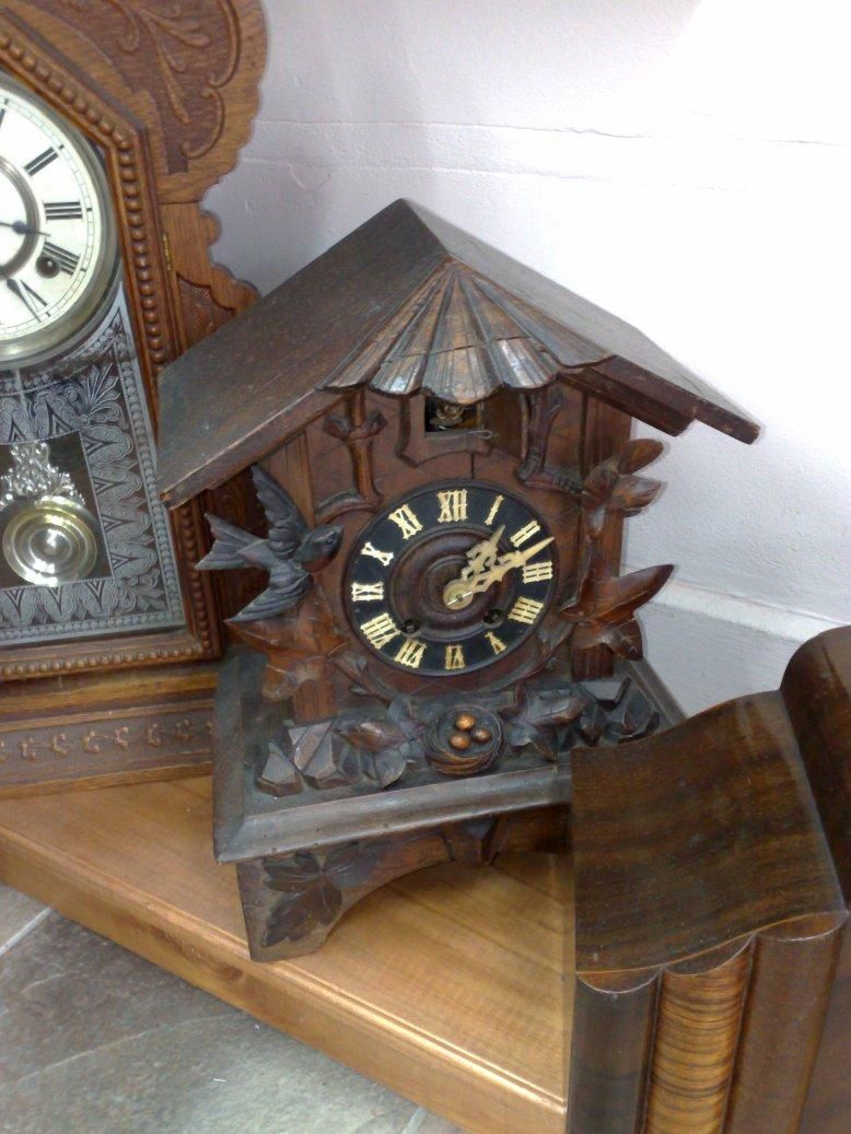 A photo of a mantle cuckoo clock in between two other clocks