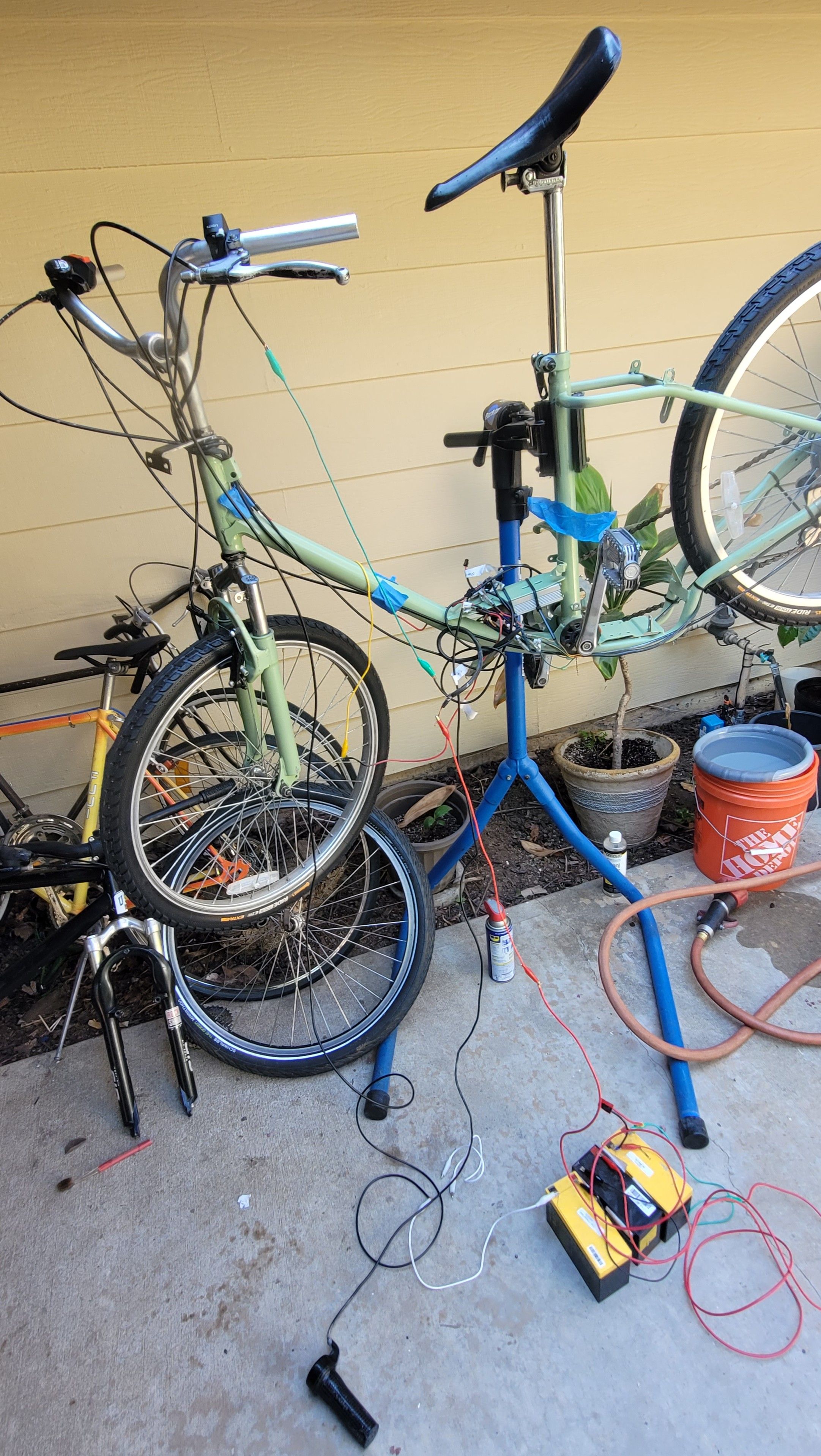 Light green ebike on a stand with SLA batteries in a pile of the floor