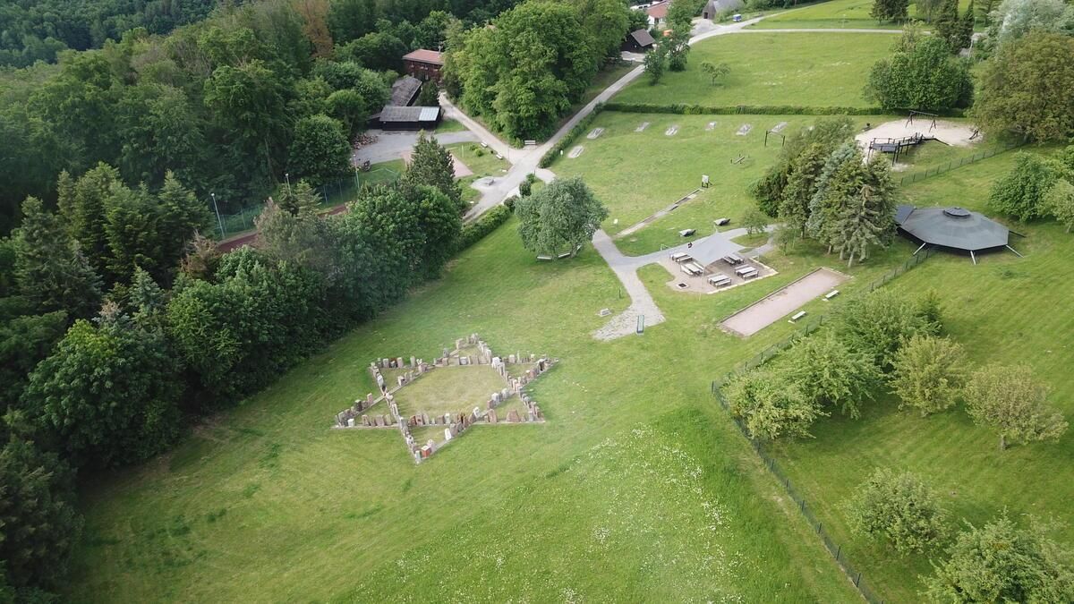 Luftbildaufnahme des zentralen Mahnmals für die am 22.10.1940 verschleppten badischen Juden. Auf einer Wiese ist ein Davidstern zu erkennen,  der aus einzelnen Gedenksteinen (aus den Deportationsorten in Baden) gebildet wird. Links ist Wald zu erkennen, rechts vereinzelt Bäume, im oberen Bereich Gebäude, die vermutlich zu der Tagungsstätte gehören.
Quelle:  www.mahnmal-neckarzimmern.de