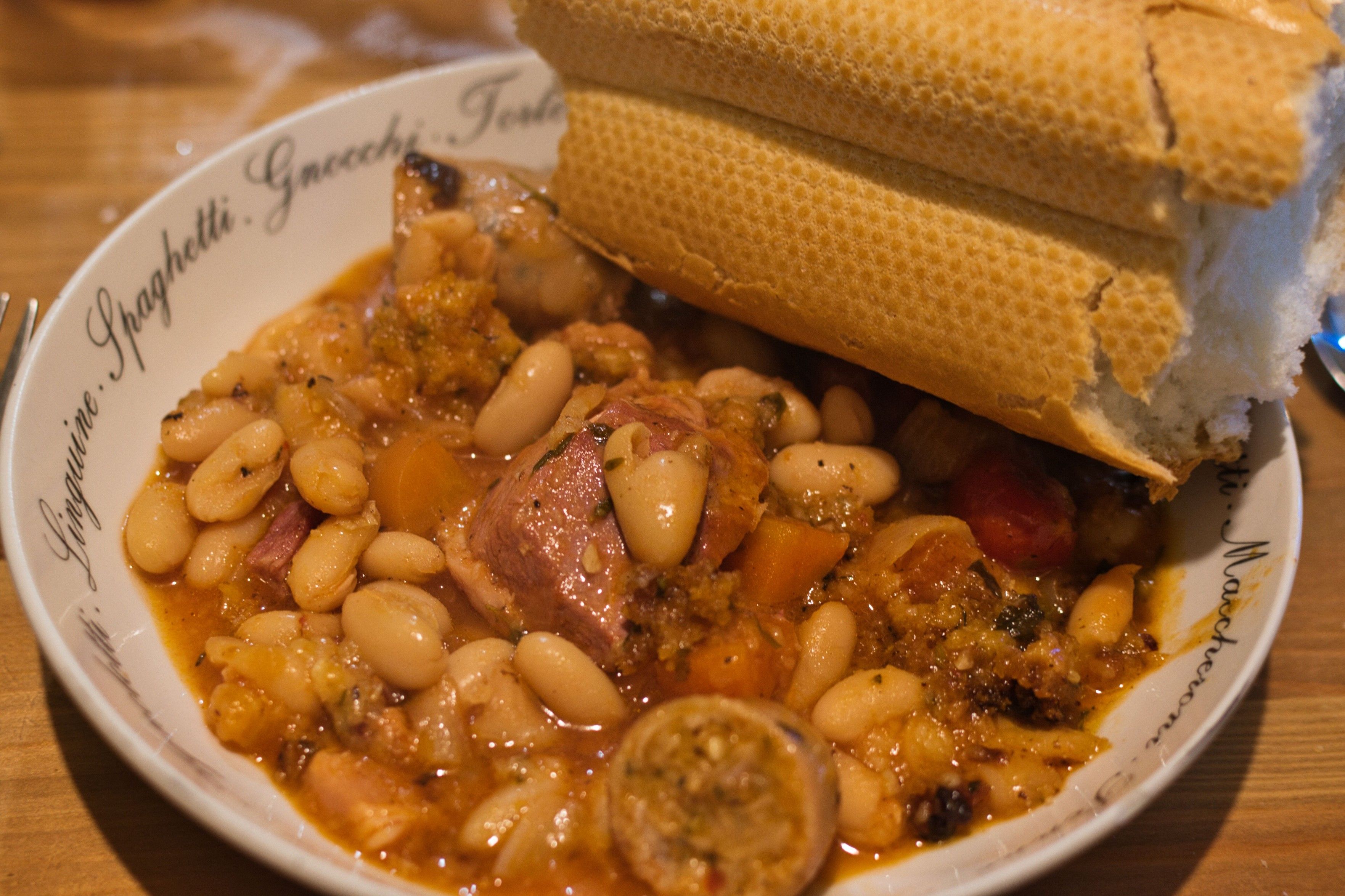 A photo of a simple cassoulet in a pasta bowl: white beans, onion, and carrot with a nice tomato based stock supporting sausage, speck, and duck breast. All with rosemary and thyme.

A decent size piece of stick bread is in the top right corner of the bowl.