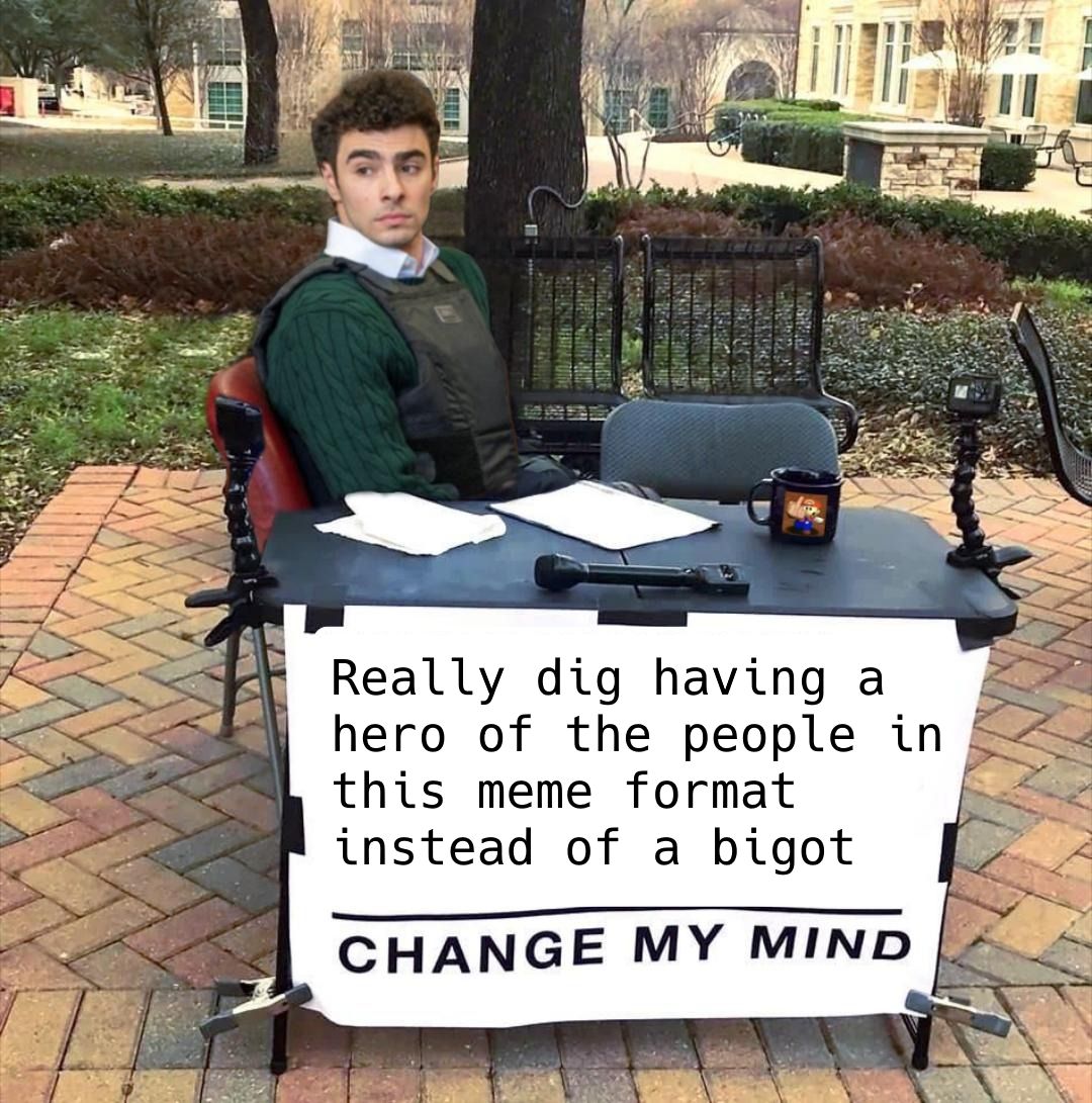 Change My Mind meme format, but the person in the chair is Luigi Mangione. Taped to the front of a table is banner that says: "Really dig having a hero of the people in this meme format instead of a bigot - CHANGE MY MIND"