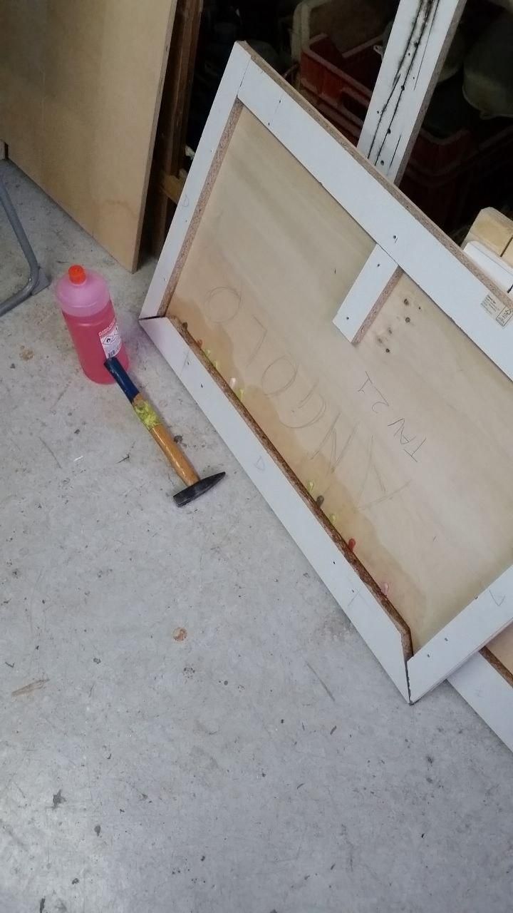 Foglio di compensato con strisce di laminato incollate sotto come irrigidimento.
A fianco una bottiglia di alcool e un martello, tra il laminato e il compensato una manciata di cunei di plastica per piastrelle.