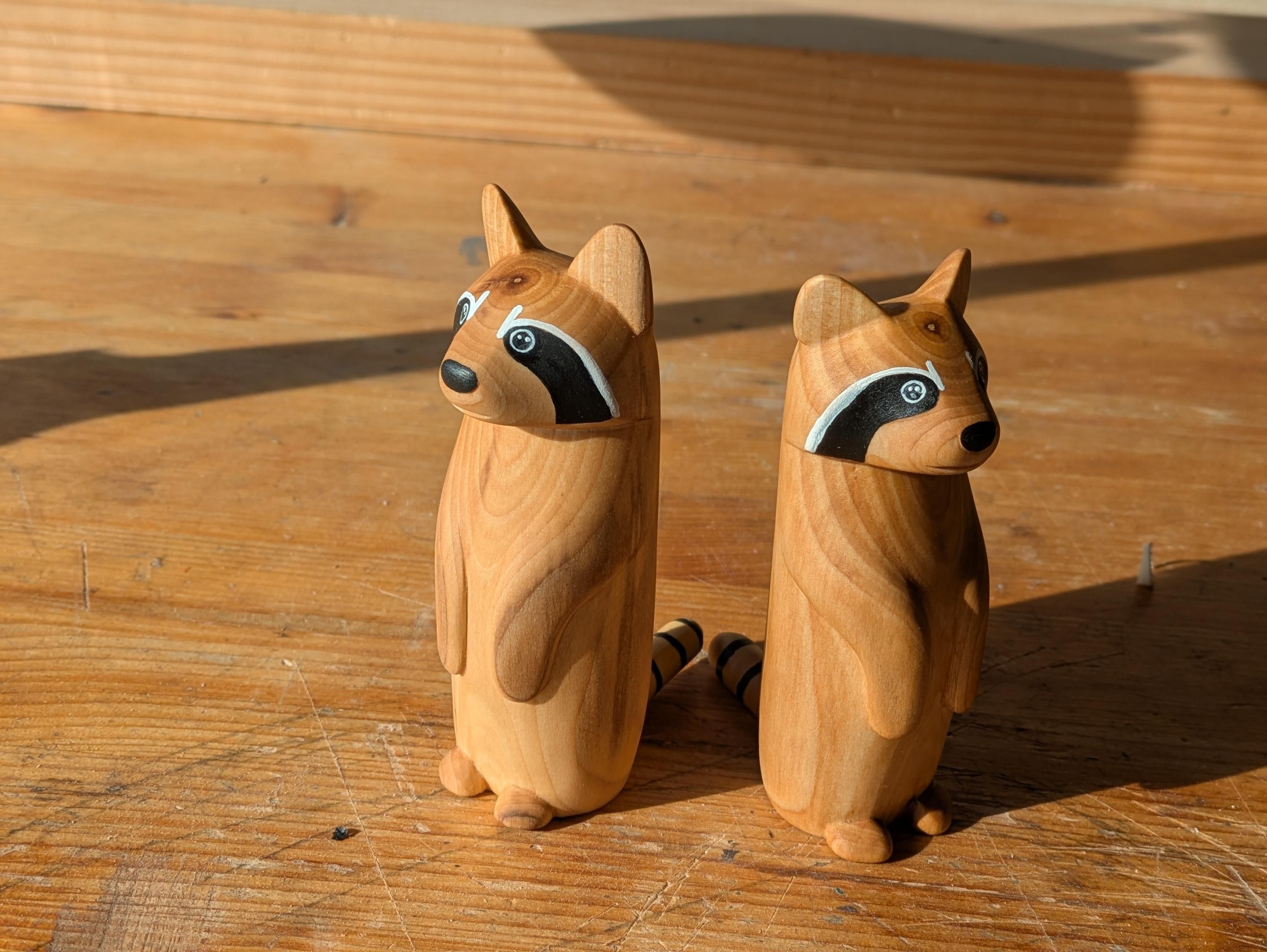 Two woodcarved raccoon on a workbench, side by side