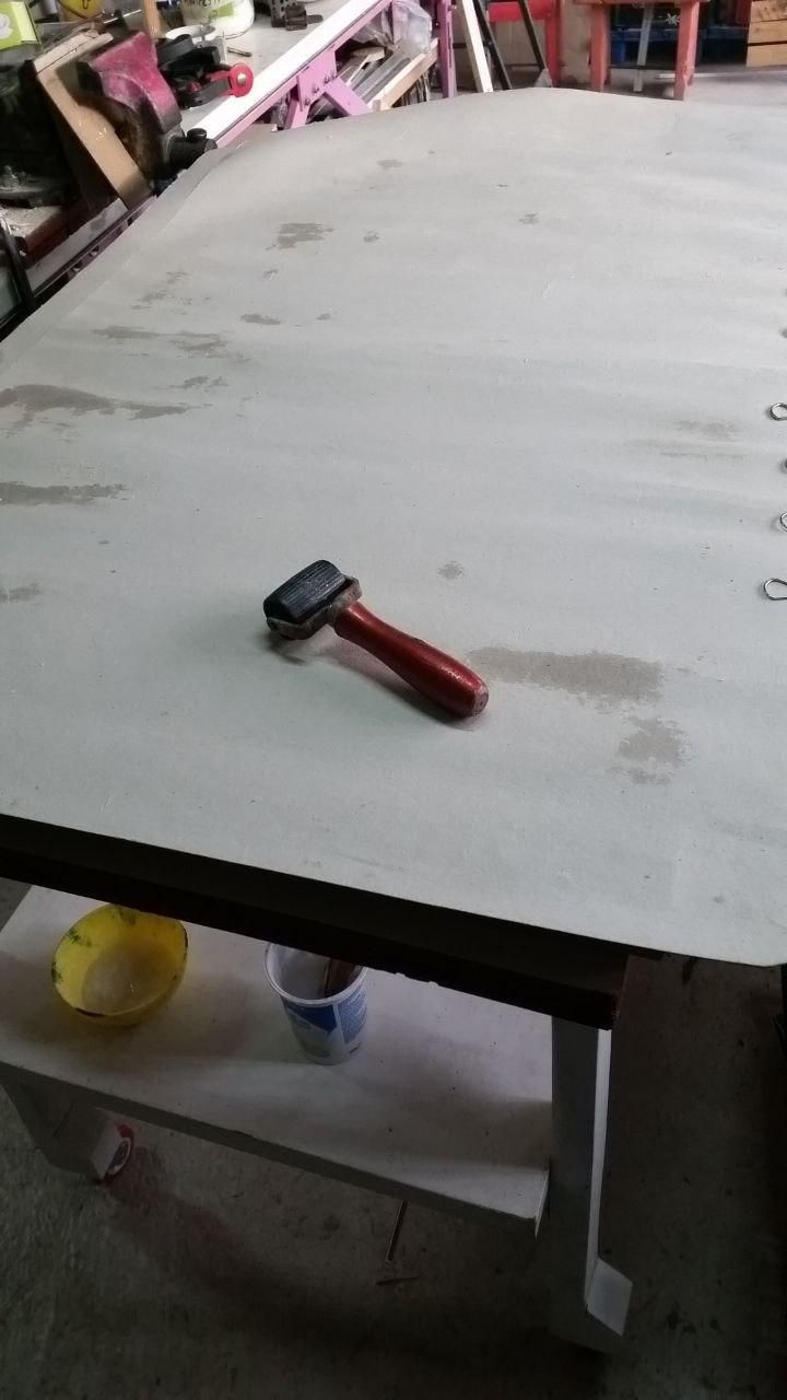 Foglio di cartone appoggiato sulla pedana da bancale, con sopra un rullino per tappezzieri.
Sul ripiano centrale una scodella gialla con la colla e un vasetto da yogurt pieno d'acqua con il pennello a bagno.