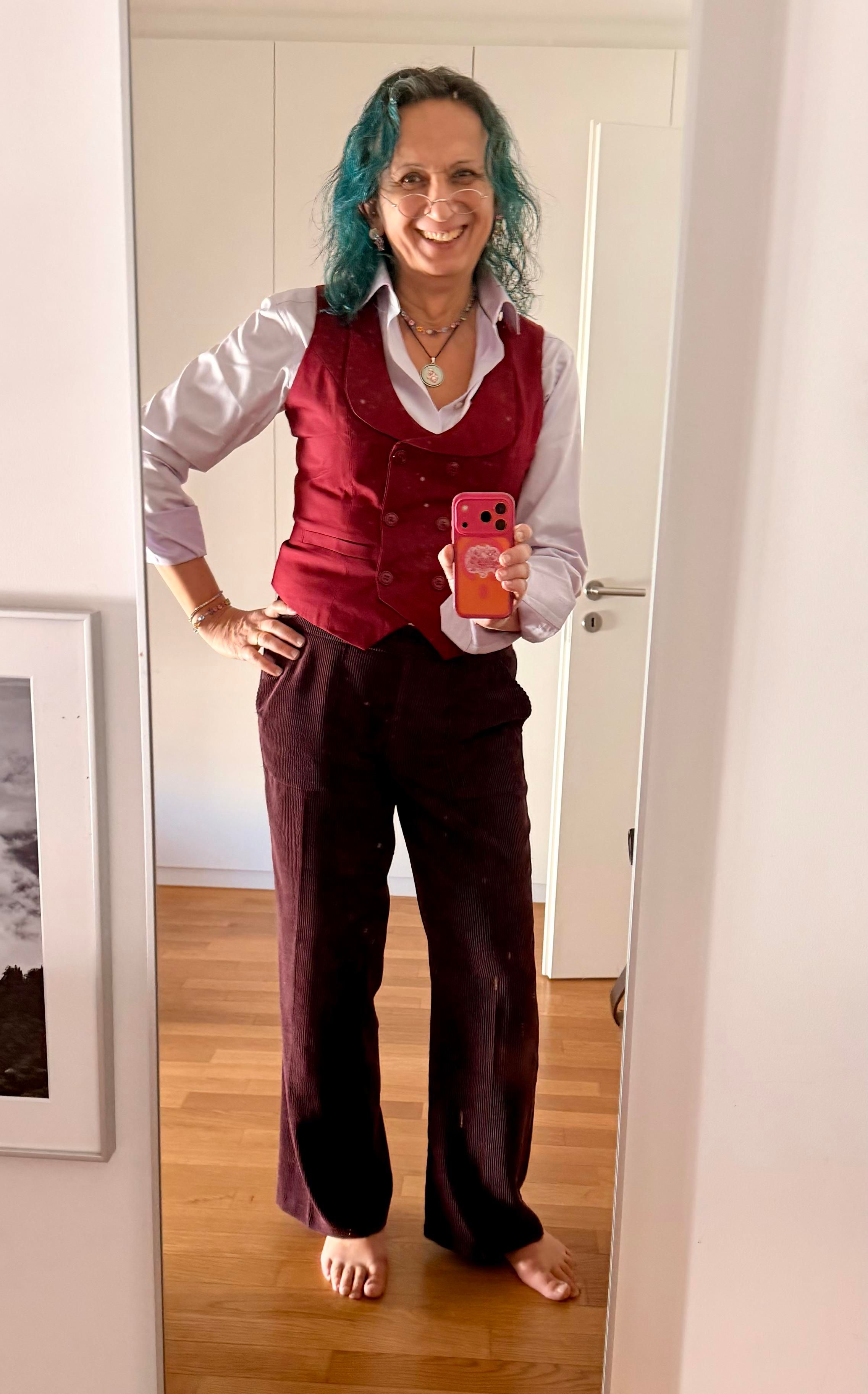 Mirror-selfie of me, a trans femme non-binary person with turquoise hair.

I am wearing a lavender shirt, a belle epoque-style wine-red vest (waistcoat), and dark-burgundy pants. 

I am also wearing my pendant with a cat all in trans colors. 

I am smiling happily. 

The whole scene looks quite serene but happy.

(Yes, yes, I am barefoot)