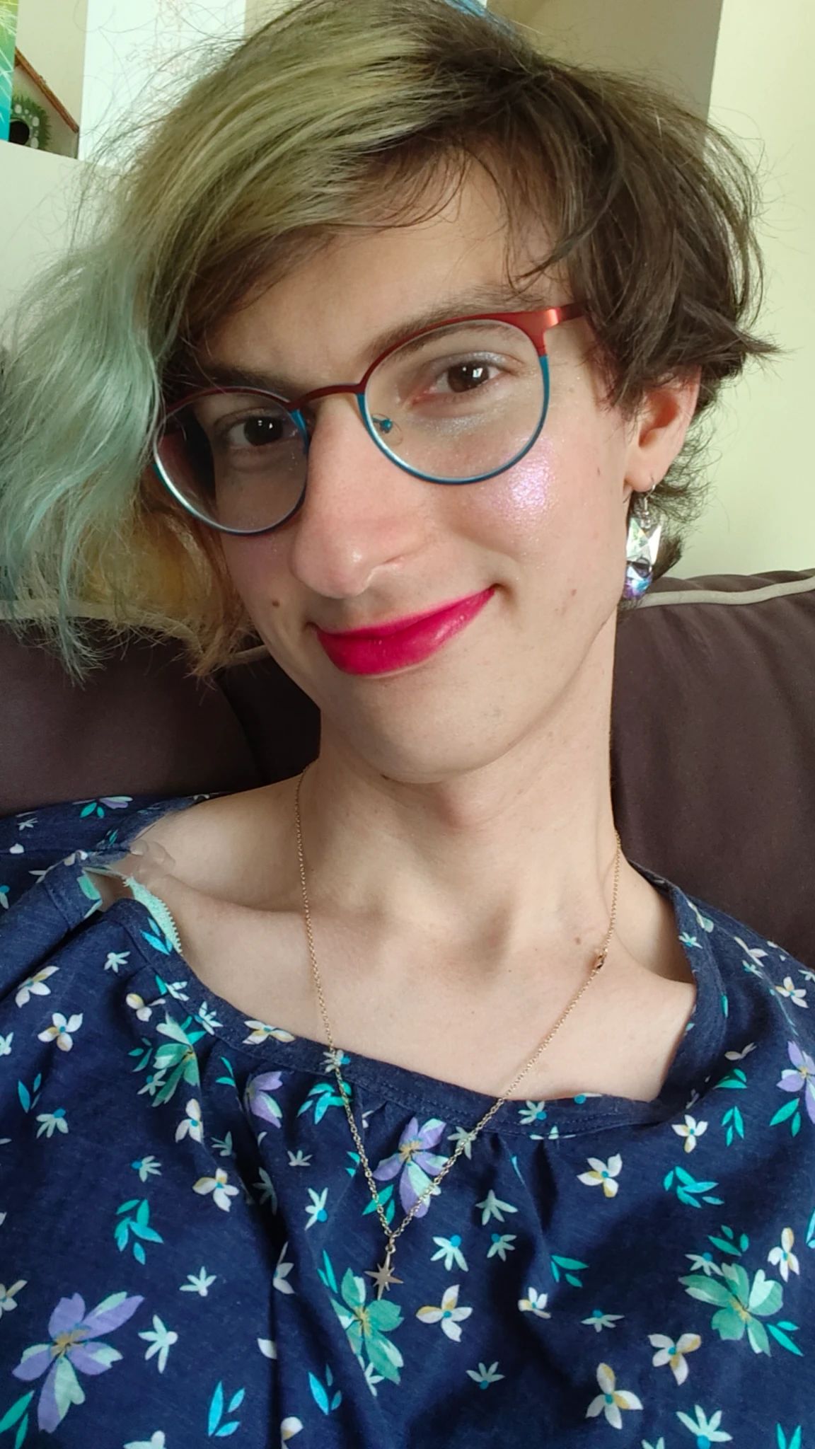 A cute white girl with blue, yellow, and pink hair.  She's wearing a blue floral top and blue and pink glasses.