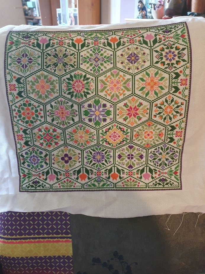 The completed Floral Hexagon cross stitch. A dark square border, inside this are multiple dark green hexagons filled with different coloured geometric flowers. 