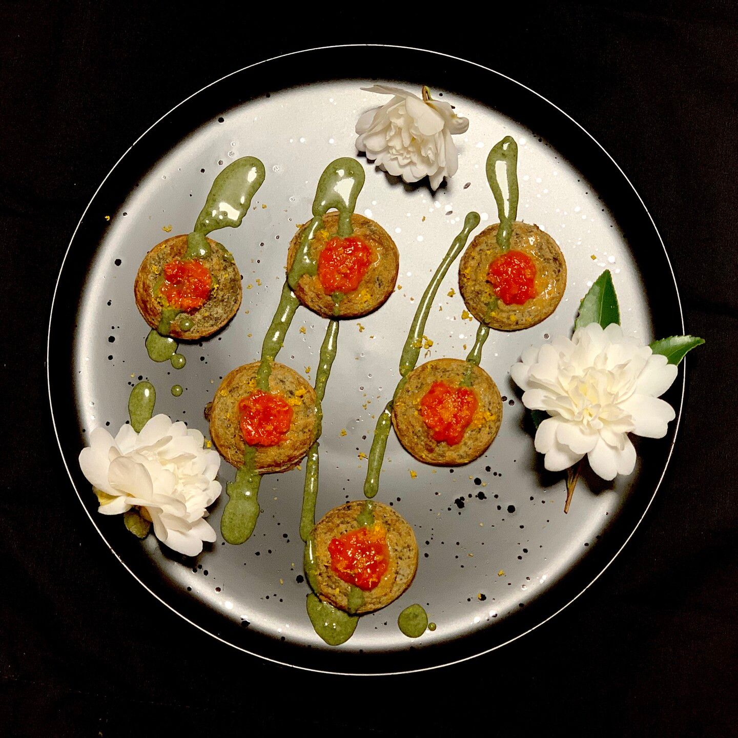 Black dish, black background, three white camellia flowers triangulate the composition on the dish. Six small pancakes the size of cookies are arranged in neat rows. Three on the top, two in the middle and one at the bottom. An inverted pyramid. On top of the of the mini pancakes is a dollop of red sauce. The pancakes have been fizzled in diagonal streaks of green sauce. Yuzu zest sprinkles complete this serene image.

Acorns change flavour the longer they are heated so I made these pancakes very small so they'd only need to be cooked for one minute on either side. They were really good. 

The red sauce was just rando fruit and veg at the moment in the garden, mad hatter peppers, yuzu juice, queen of minalco tomatillo, strawberry, and tiny bit of ketchup, pinch salt and sugar. Very tasty.

Green sauce was sissoo leaf powder, vegan yogurt, pinch salt and sugar and later mixed a bit of water for drizzle-ability. 