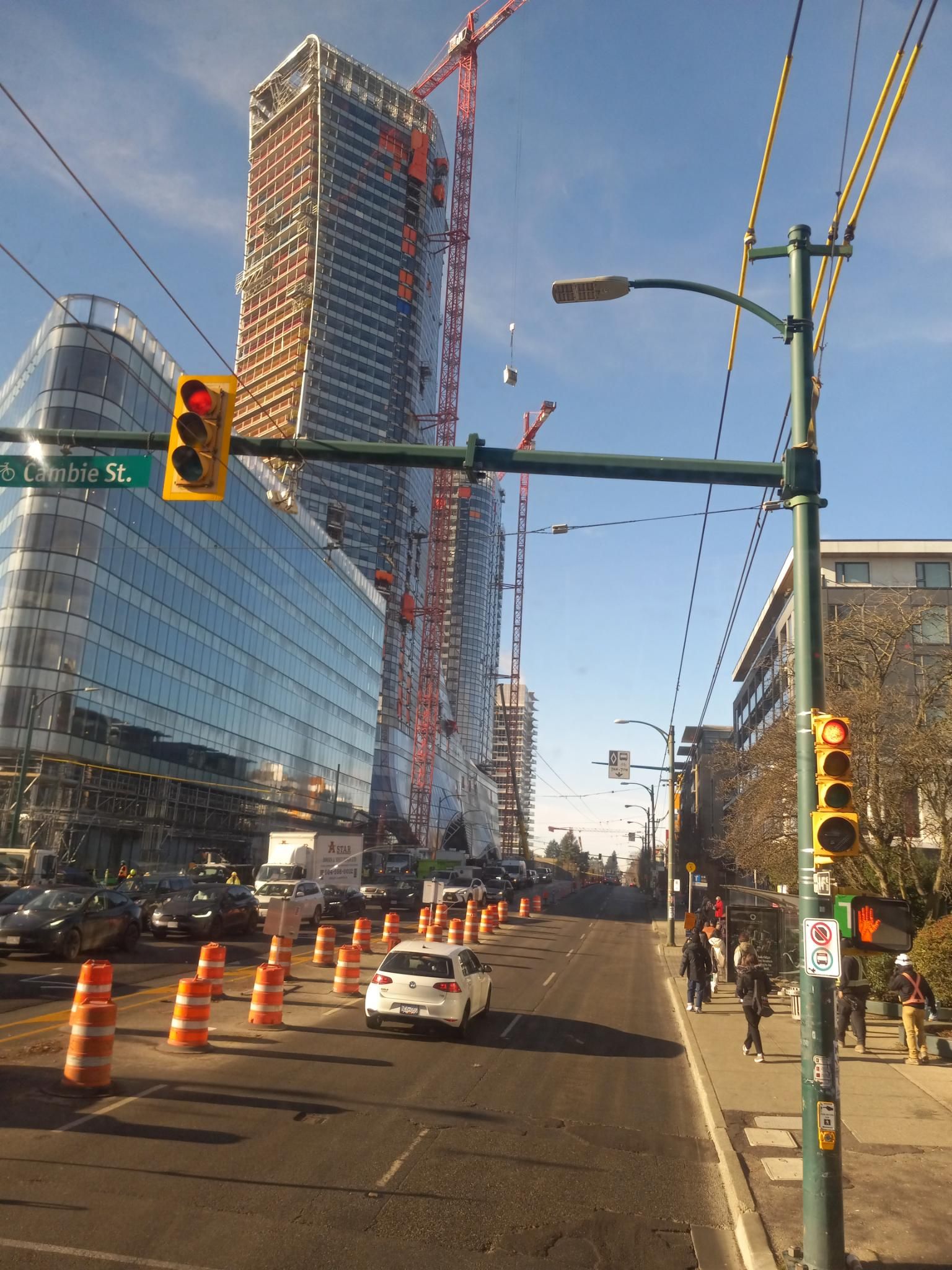 A view down 41st street with a bunch of gigantic high rises under construction, with huge cranes lifting things into the air.  The sky is blue and it's sunny, and there are a lot of road cones along the side of the road.