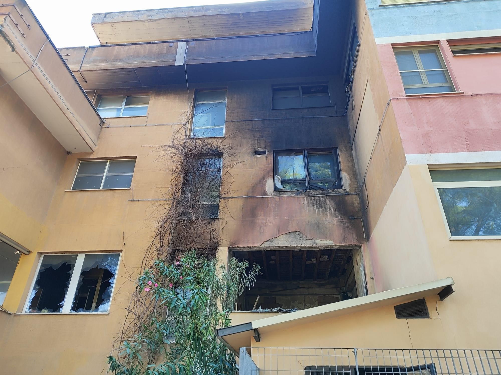 Palazzina di 2 piani color giallo ocra con facciata bruciata e finestre rotte