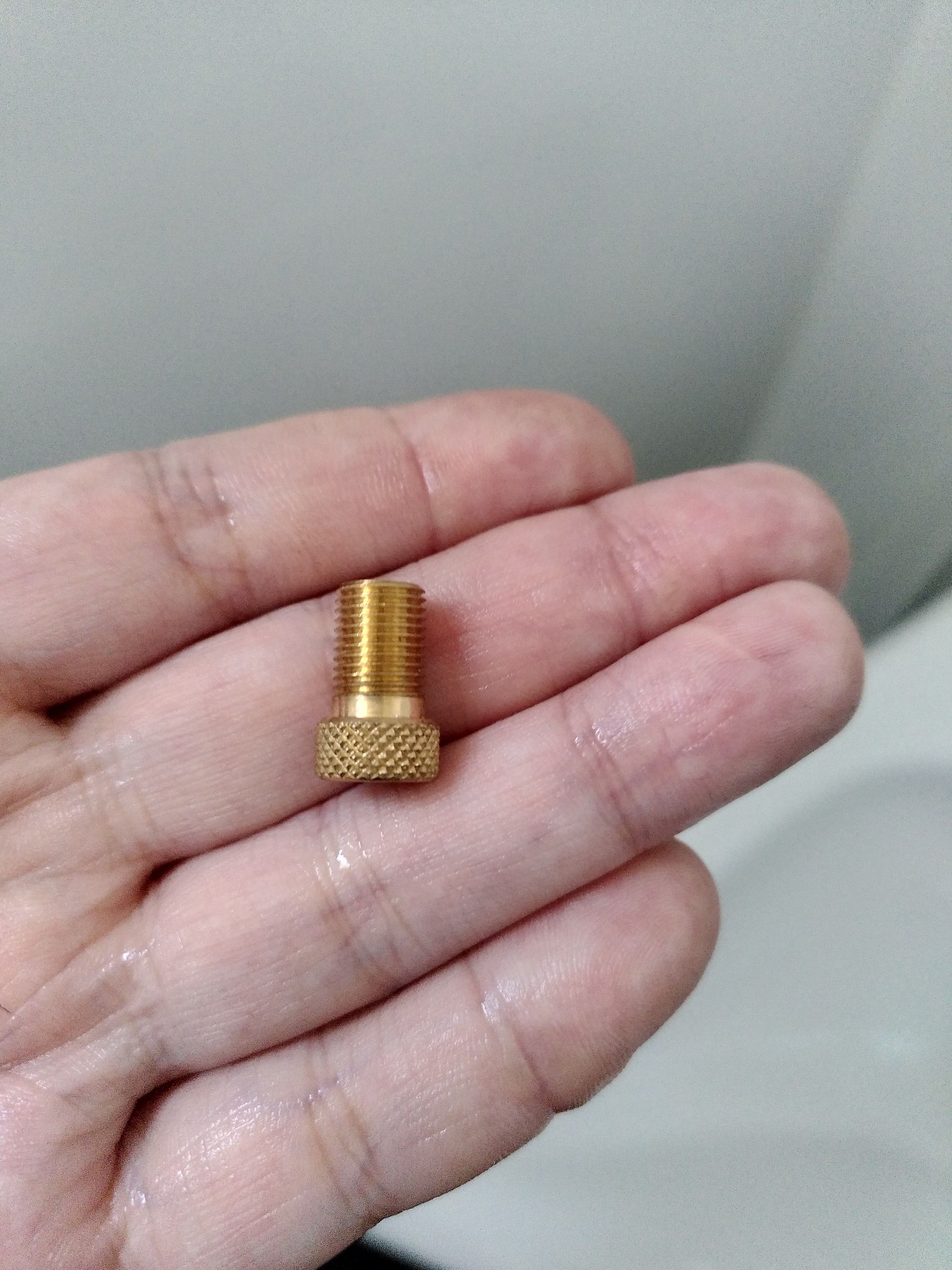 A Schraeder to presta adapter being held on four fingers.