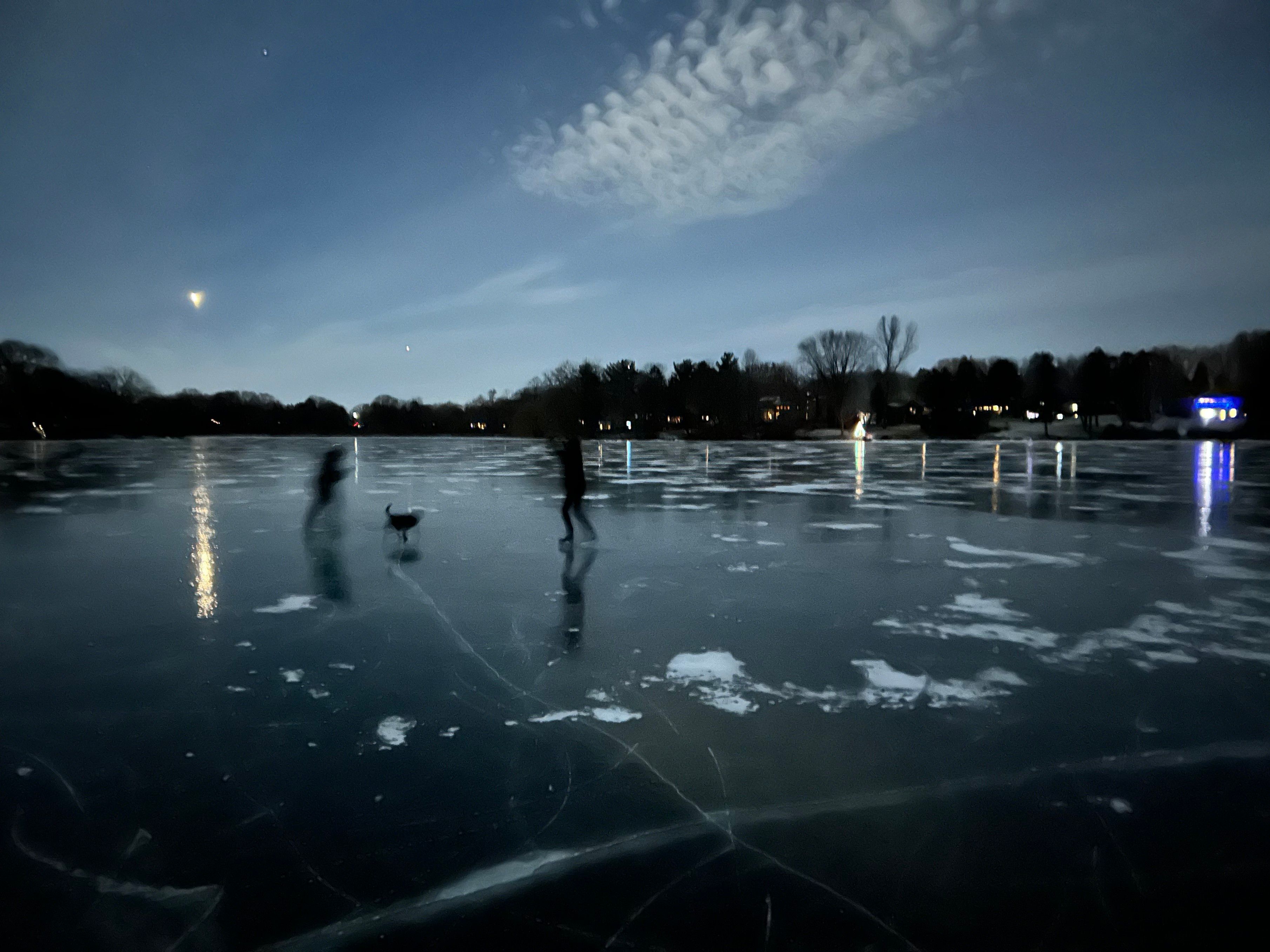 Nighttime skate on a lake. 2 silhouettes of people and one of a dog. 