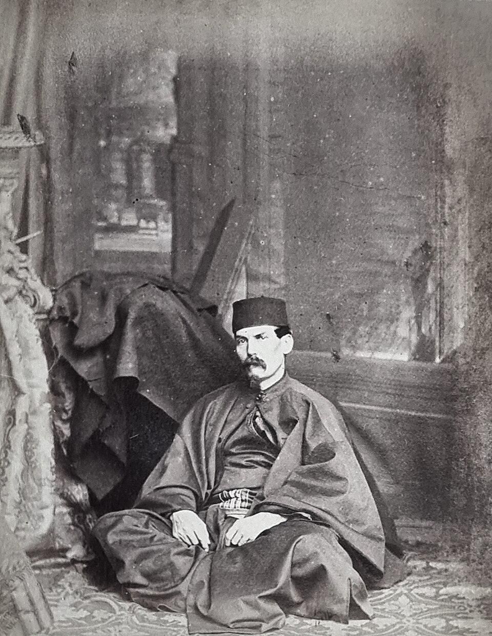 Portrait of Captain Richard Burton, British explorer, army officer, orientalist writer and scholar, c. 1863, by Ernest Edwards, from vintage albumen print in the publication Portraits of Men of Eminence in Literature, Science, and Art, with Biographical Memoirs, Edwards, Ernest, and Lovell Reeve, State Library of New South Wales, DSM/920.042/P

Burton is dressed in Middle Eastern/Ottoman attire:
Fez or tarbush (traditional cap)
Flowing robes and kaftan
Sash around the waist
Dagger visible at his waist
Oriental setting: Seated on cushions with draped fabric and tent-like backdrop
His characteristic intense gaze and prominent mustache
A pose suggesting his famous ability to "pass" as a native in various cultures

https://upload.wikimedia.org/wikipedia/commons/thumb/0/03/Edwards_Richard_Burton_1864_slnsw.jpg/960px-Edwards_Richard_Burton_1864_slnsw.jpg