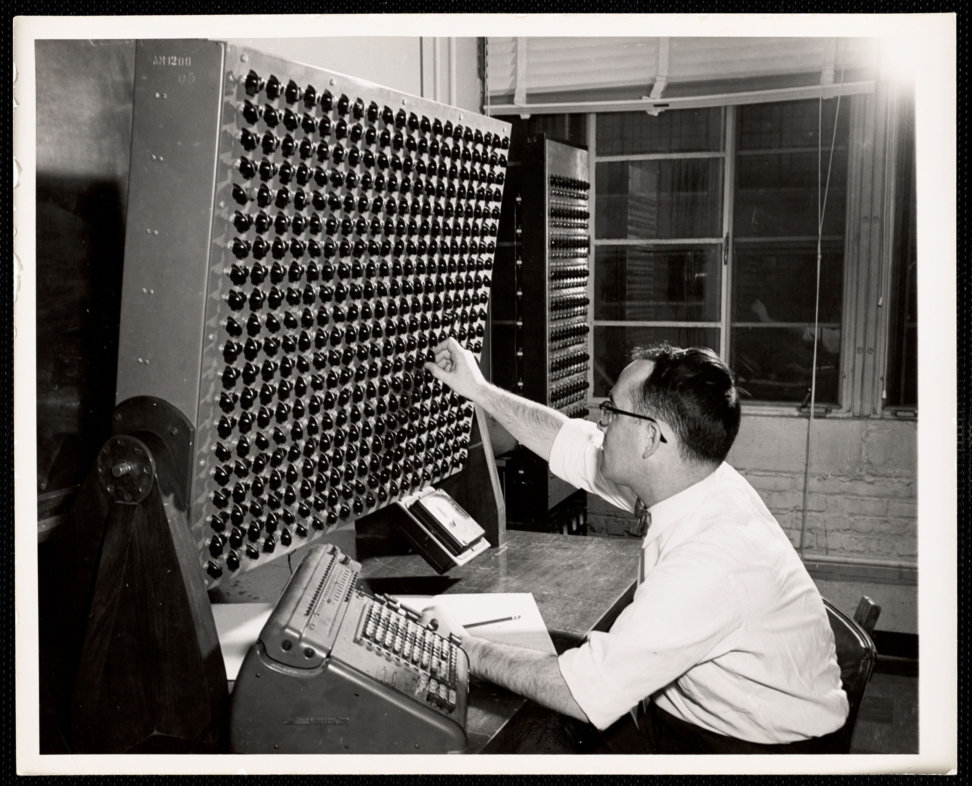 A man operating a large analogue computer in an office.